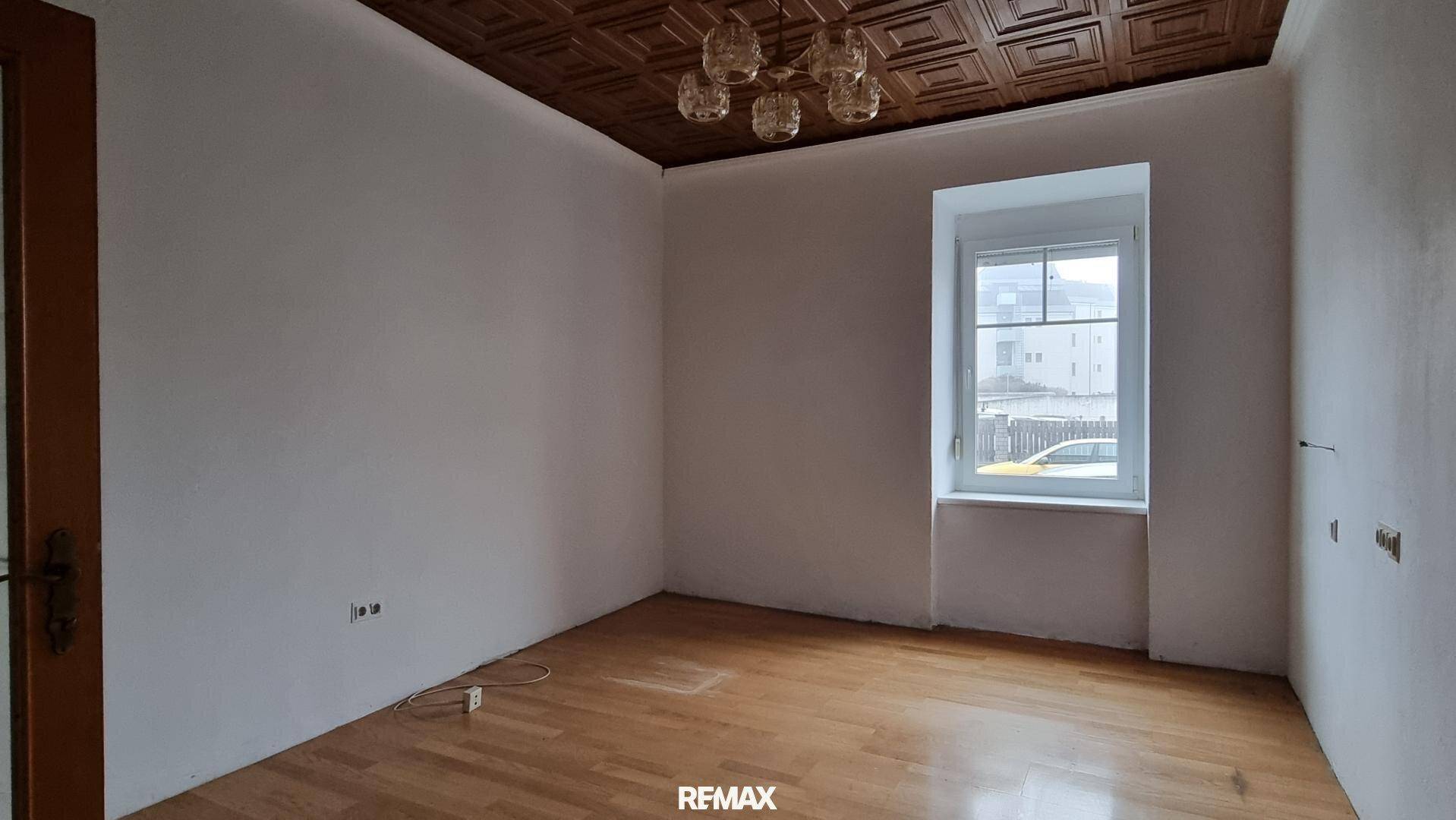 Geräumiges Zimmer mit Holzboden, dekorativer Decke und einem Fenster zur Straße, klassisch eingerichtet.