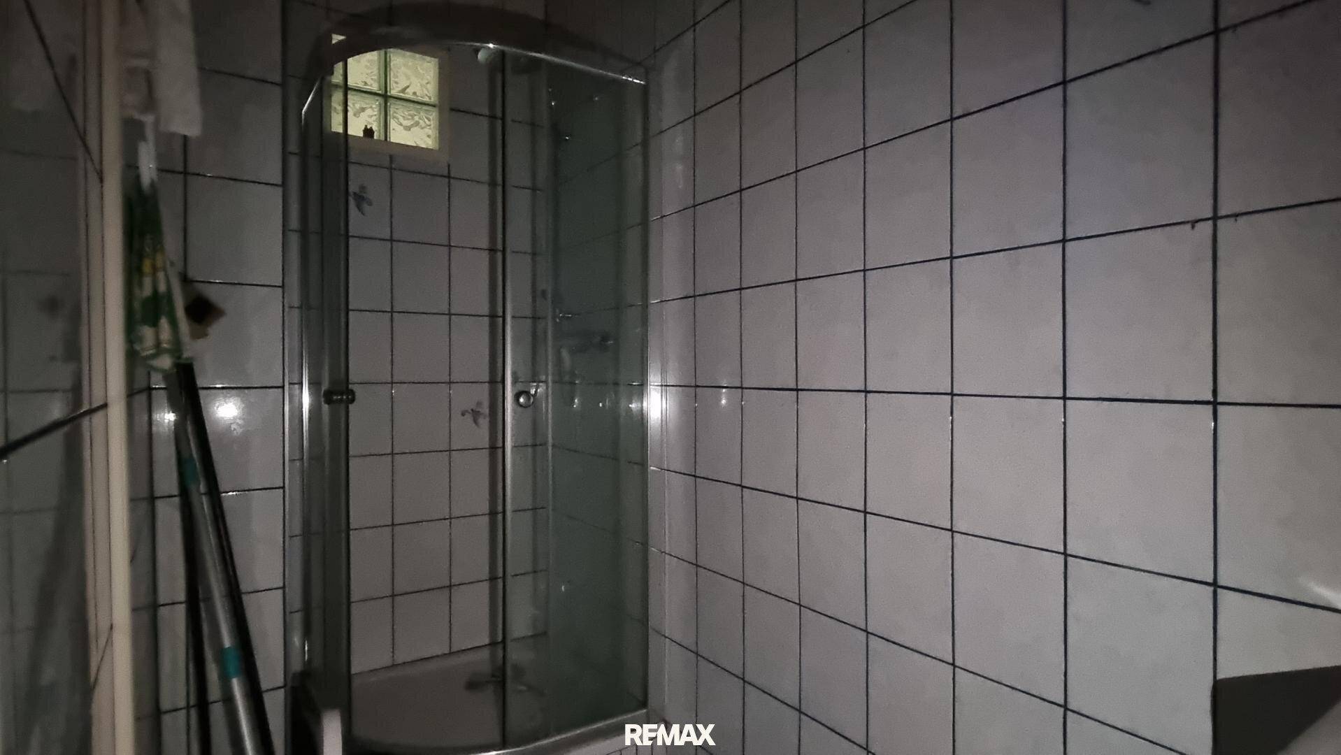 Badezimmer mit weißen Fliesen und einer Duschkabine, die auf Renovierung wartet oder einfach gehalten ist.