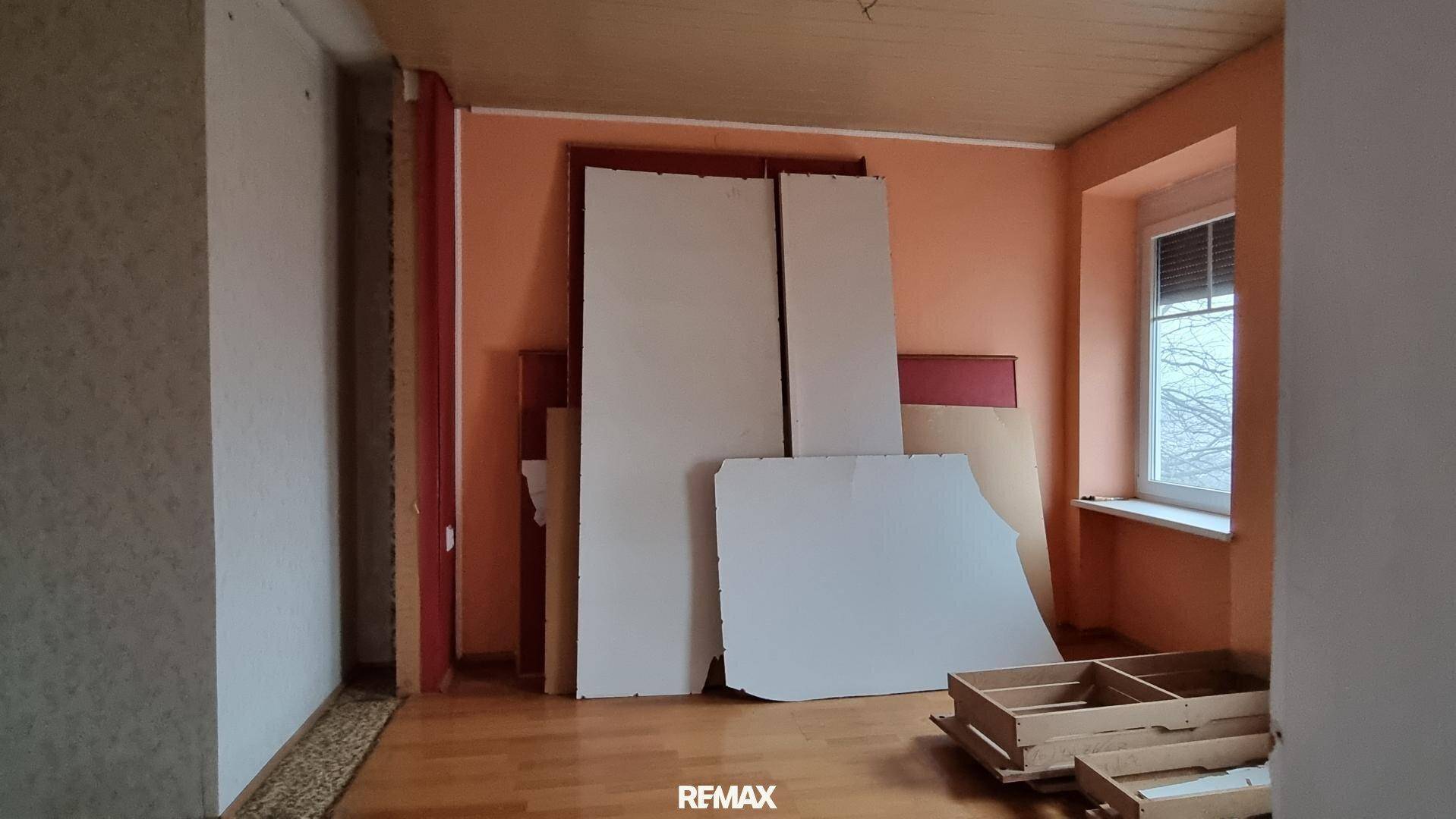 Zimmer mit orangefarbenen Wänden, Holzboden und Baumaterialien, die auf den Einbau warten.
