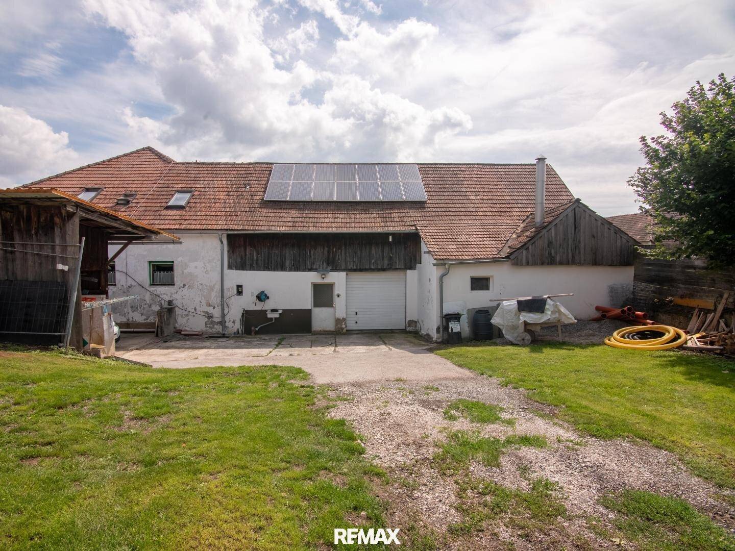 Rückansicht eines Gebäudes mit Photovoltaikanlage auf dem Dach und großem Rasenbereich.