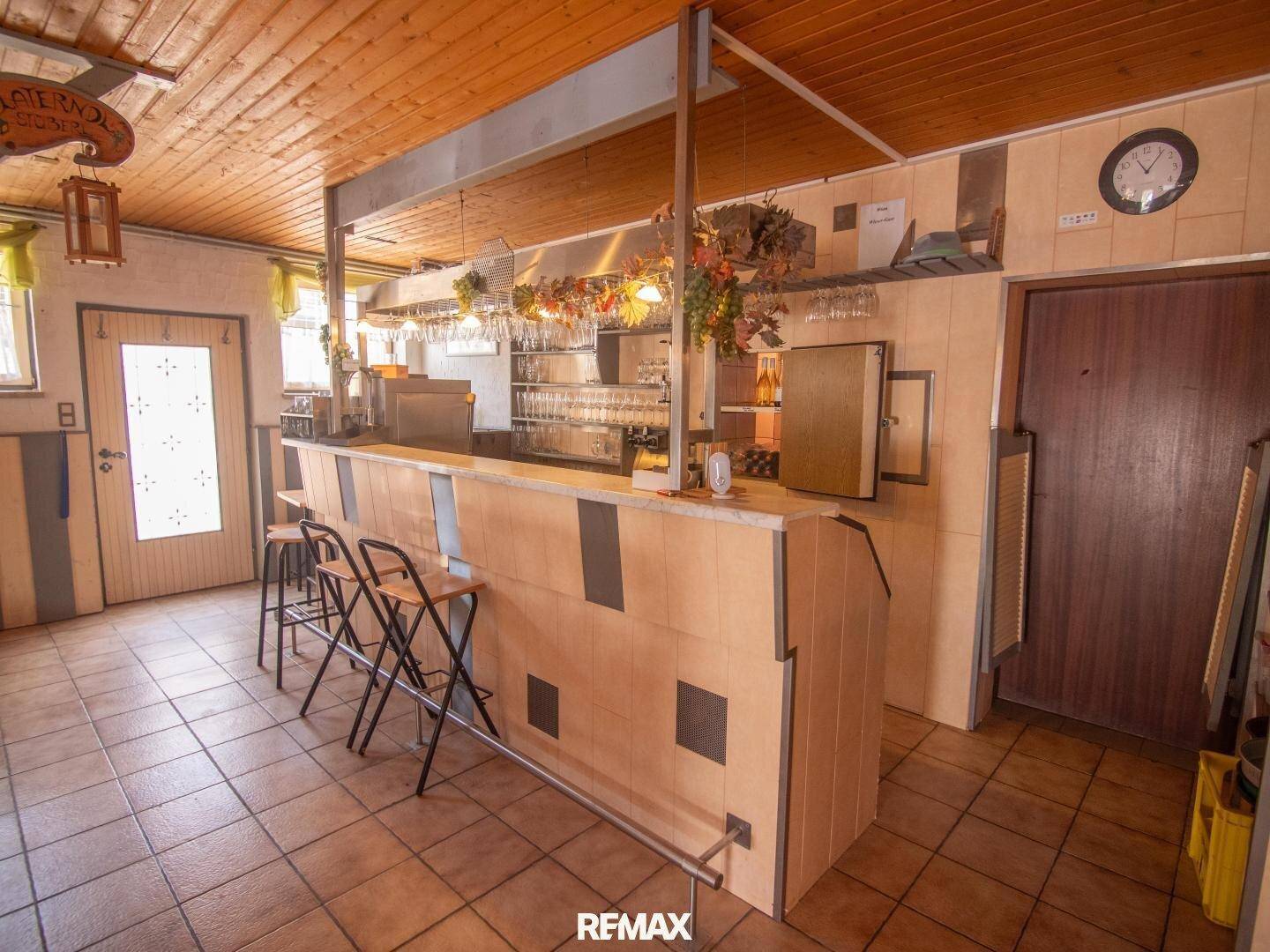Bar im Wohnbereich mit Hockern und Gläserregal, umgeben von rustikaler Holzvertäfelung.