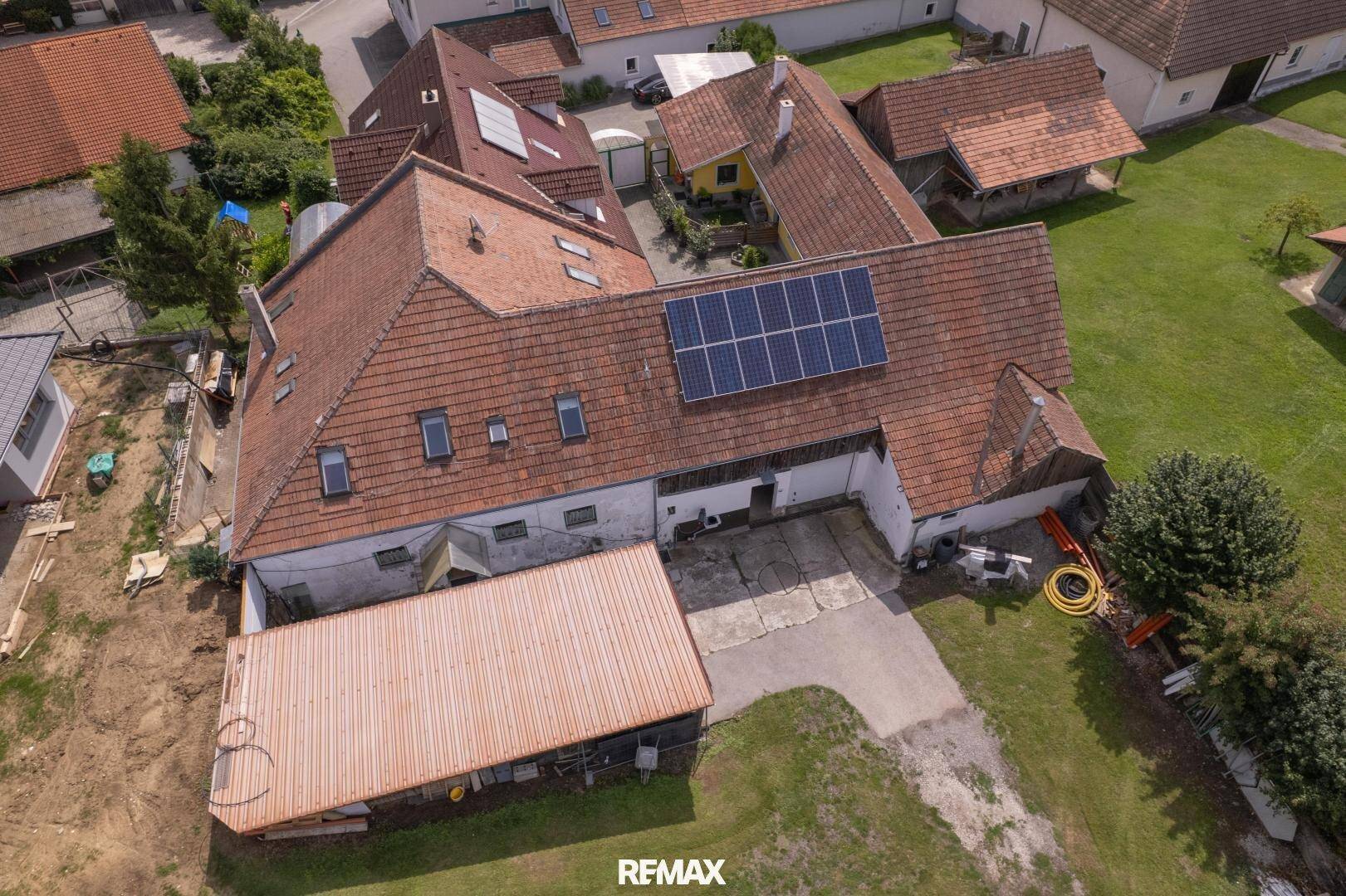 Vogelperspektive eines weitläufigen Anwesens mit Photovoltaikanlagen auf den Dächern und Grünflächen.