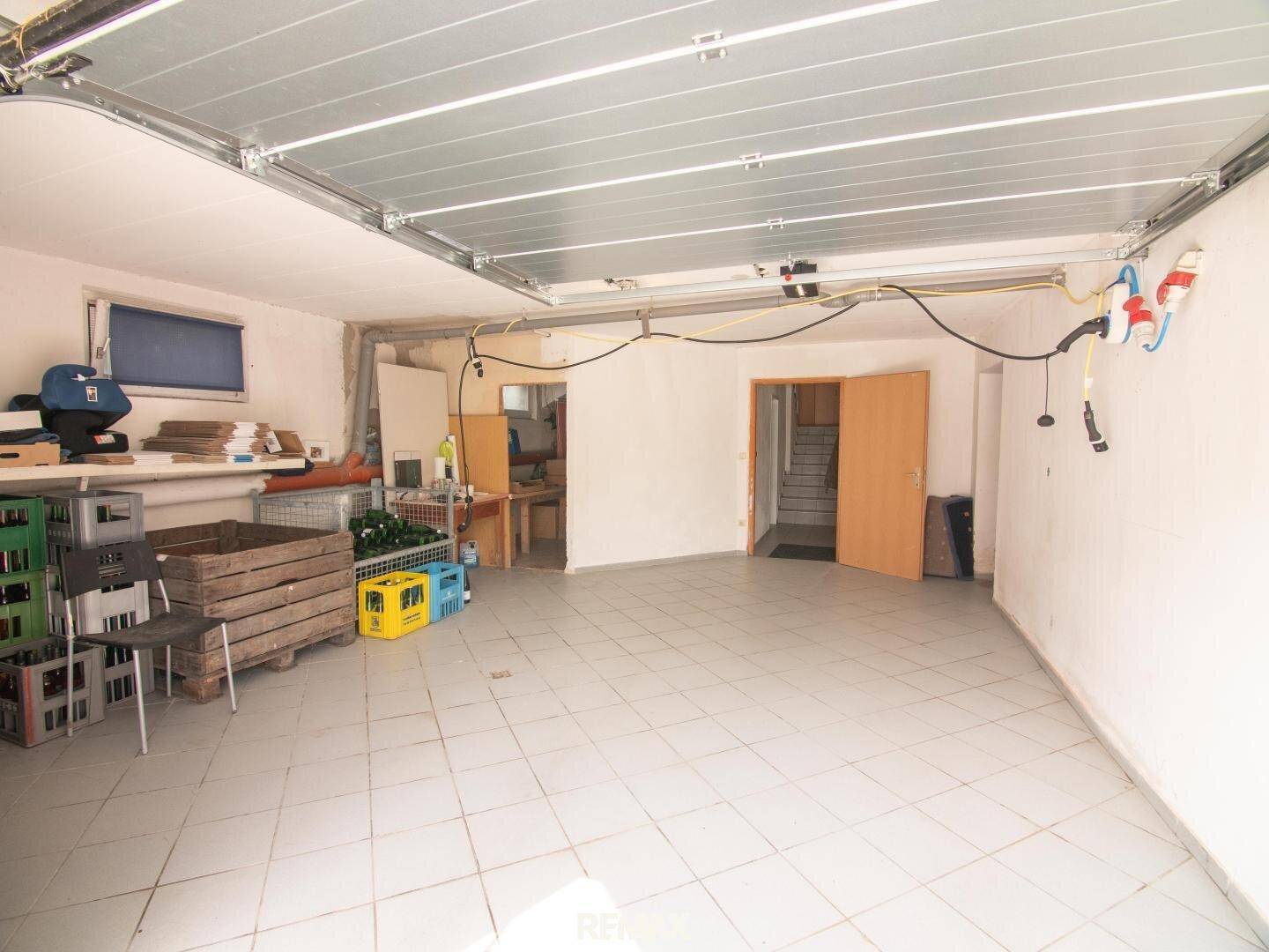 Saubere Garage mit Fliesenboden und Zugang zu weiteren Räumen, ideal für Fahrzeuge und Lagerung.