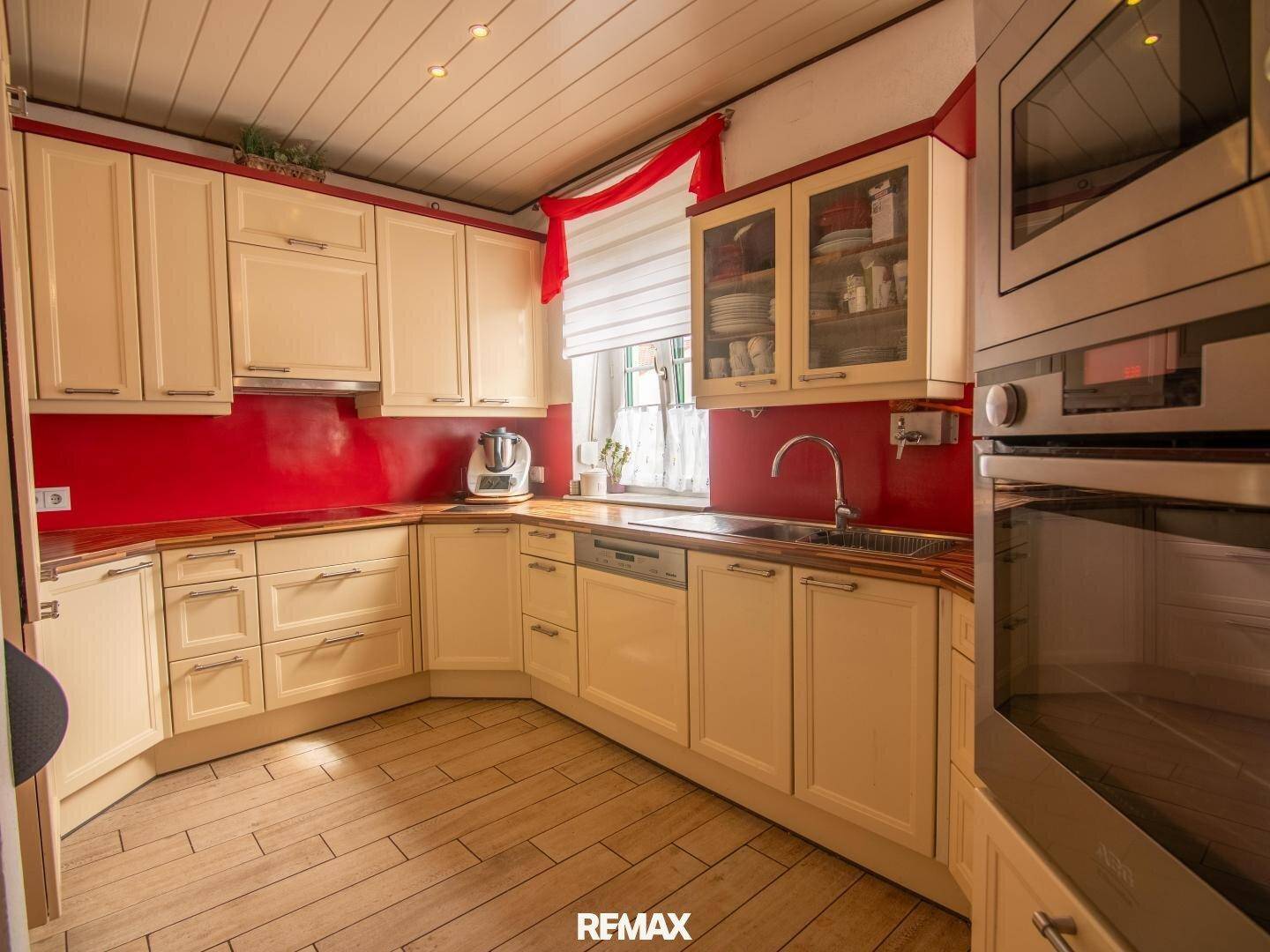 Traditionelle Küche mit cremefarbenen Schränken, roter Rückwand und Holzbalkendecke.