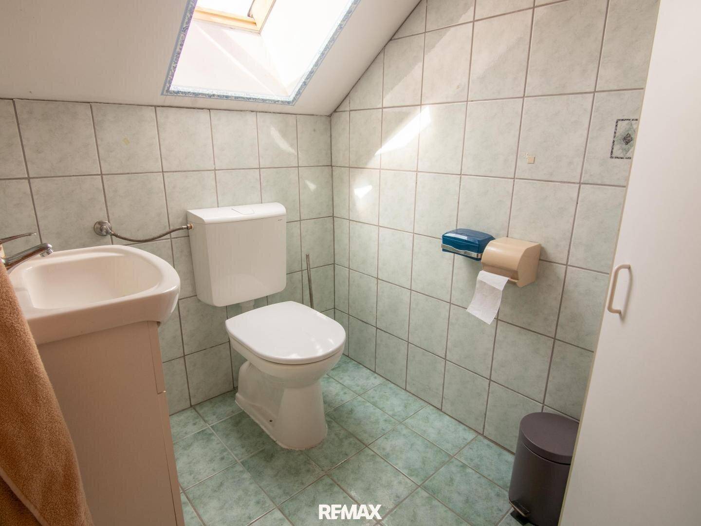 Separates WC mit Toilette, kleinem Waschbecken und Dachfenster.