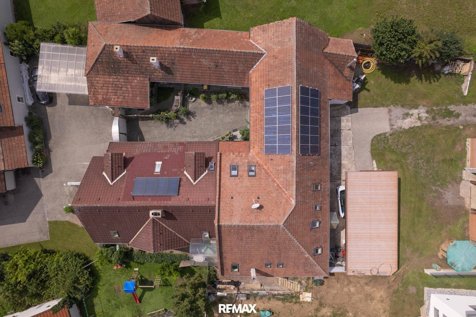 Gesamtansicht des Anwesens von oben, mit mehreren Dächern, Photovoltaikanlagen und einem Spielplatz.