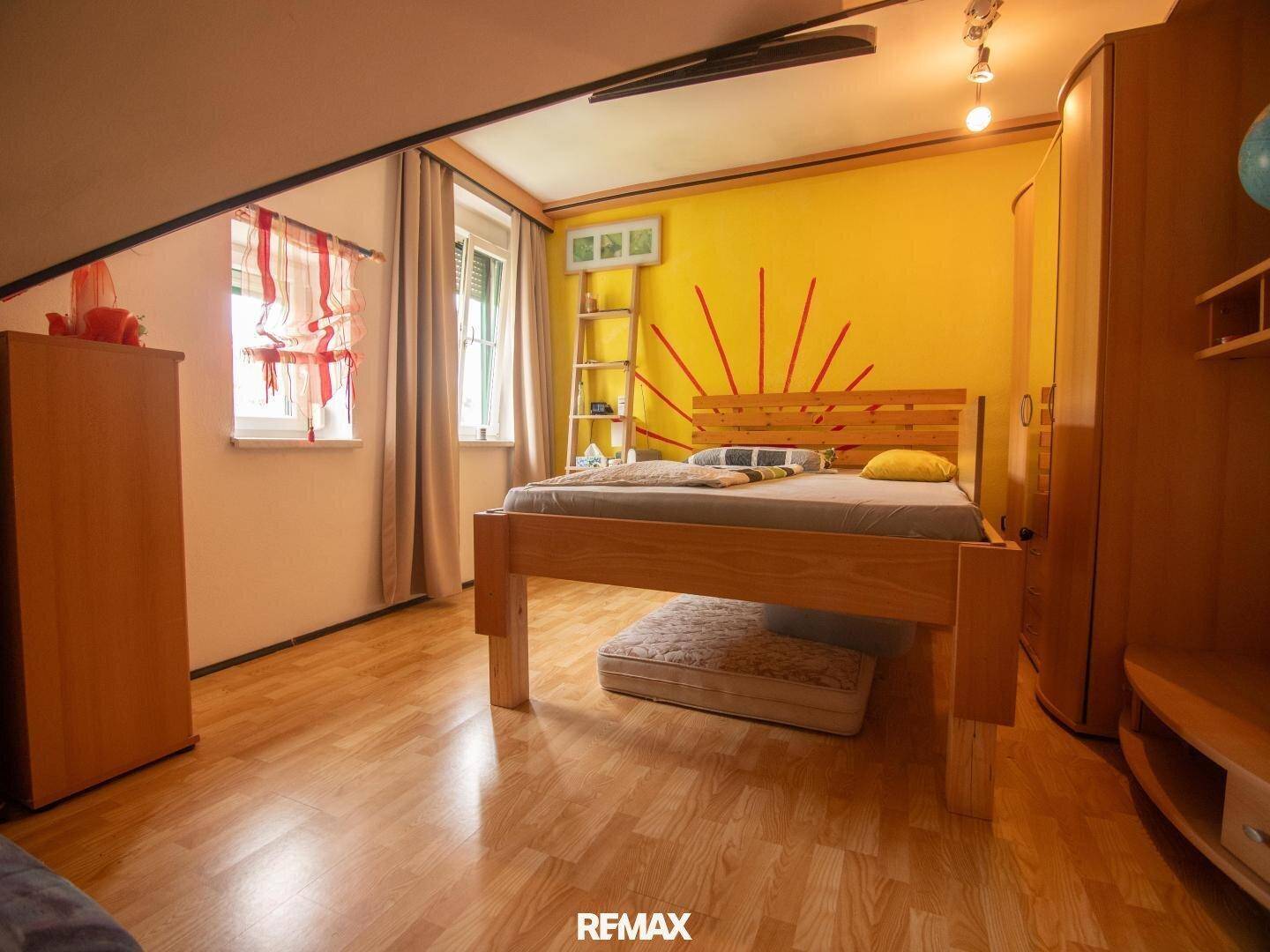 Helles Schlafzimmer mit Einzelbett, Holzboden und Dachschräge.