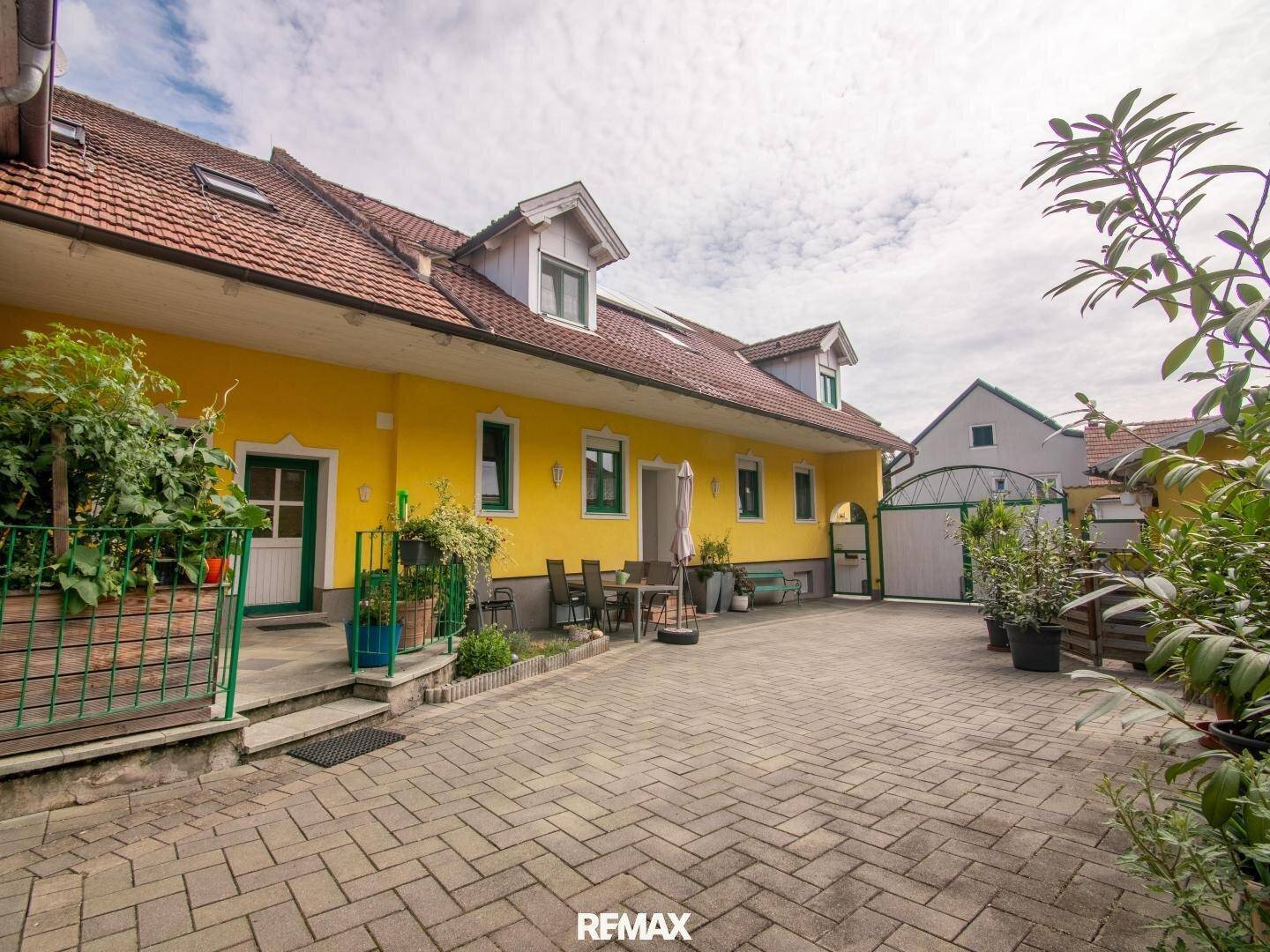 Ansicht des gelben Gebäudes mit gepflastertem Hof und Sitzbereich im Freien.