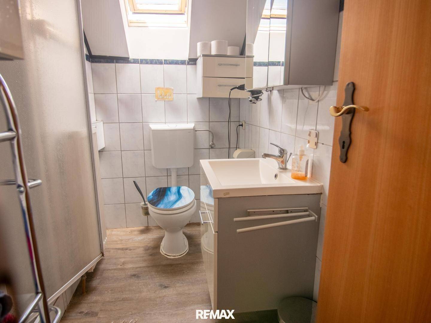 Badezimmer mit Dusche, Toilette, Waschbecken und Dachfenster.