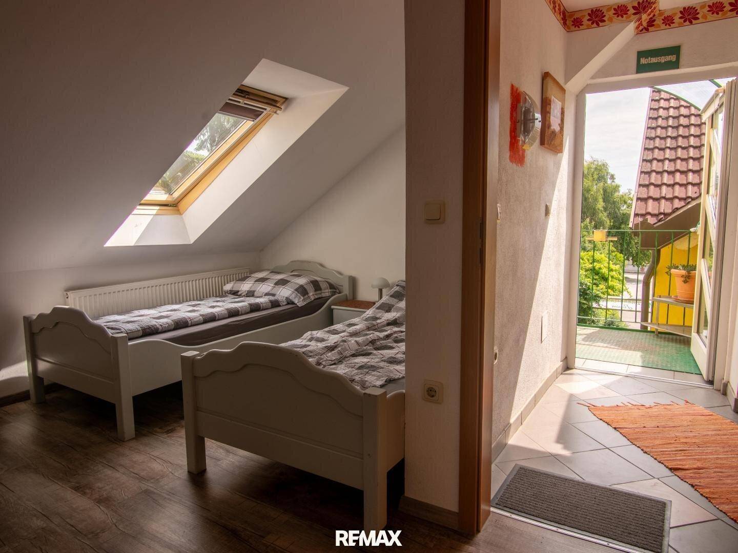 Schlafzimmer mit zwei Betten, Holzboden, Dachfenster und Balkonzugang.