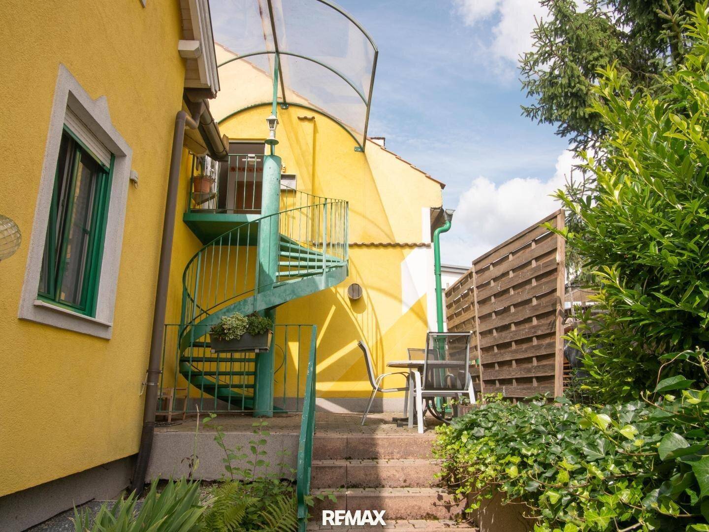 Grüne Wendeltreppe an der gelben Fassade, die zu einem oberen Stockwerk führt.