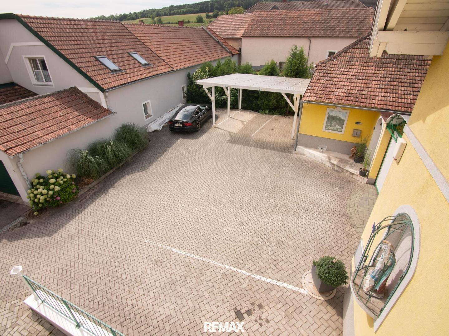 Großer gepflasterter Hofbereich mit Parkplätzen und einem Carport, umgeben von Wohnhäusern.