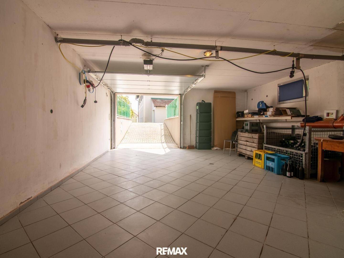 Helle Garage mit Fliesenboden und offenem Tor, das den Blick auf die Auffahrt freigibt.