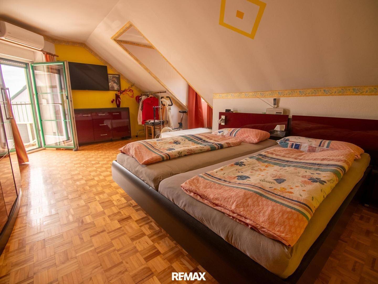 Schlafzimmer im Dachgeschoss mit zwei Betten, Holzboden und Zugang zum Balkon.