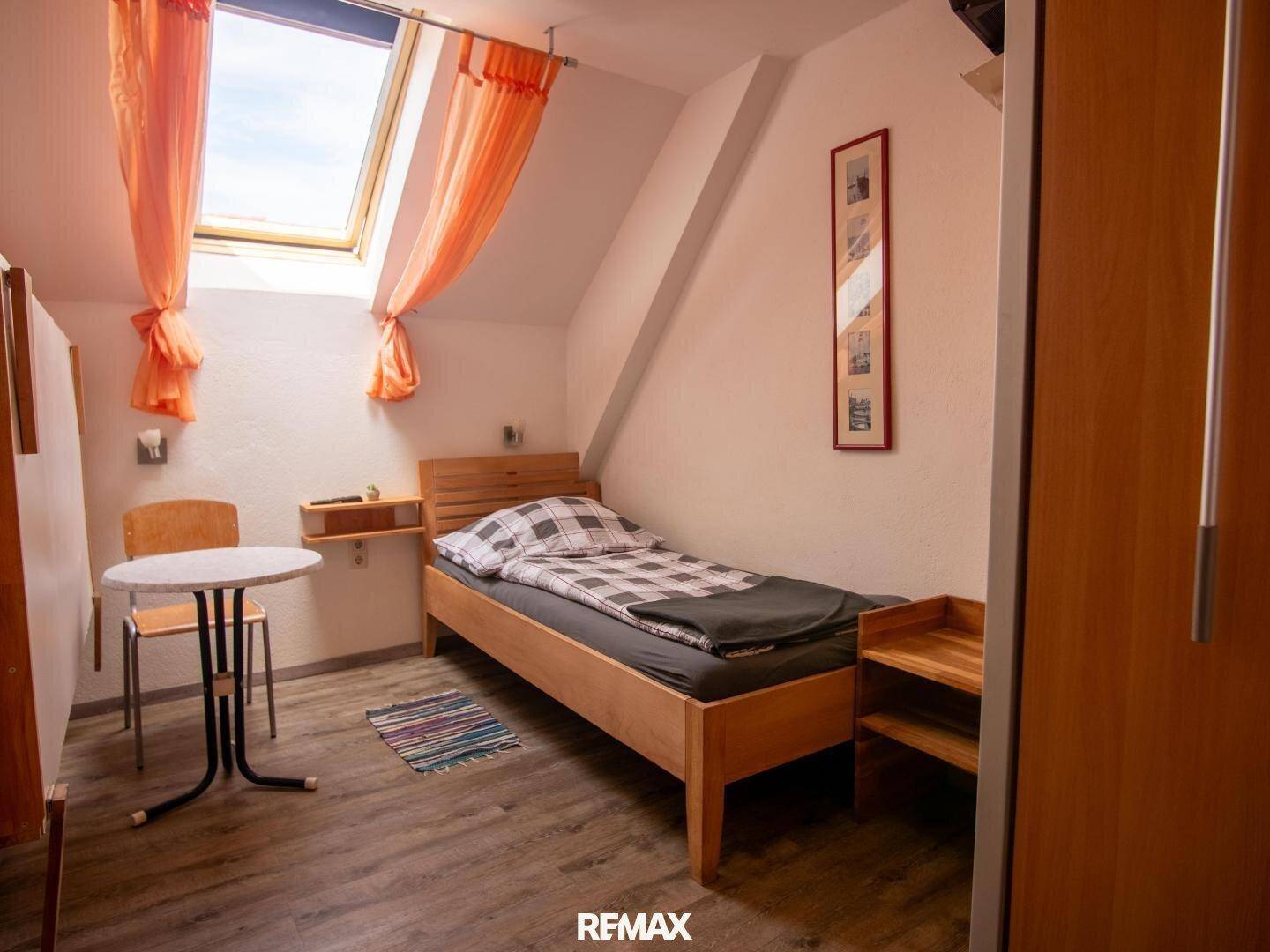 Helles Schlafzimmer mit Einzelbett, kleinem Tisch und Dachfenster.