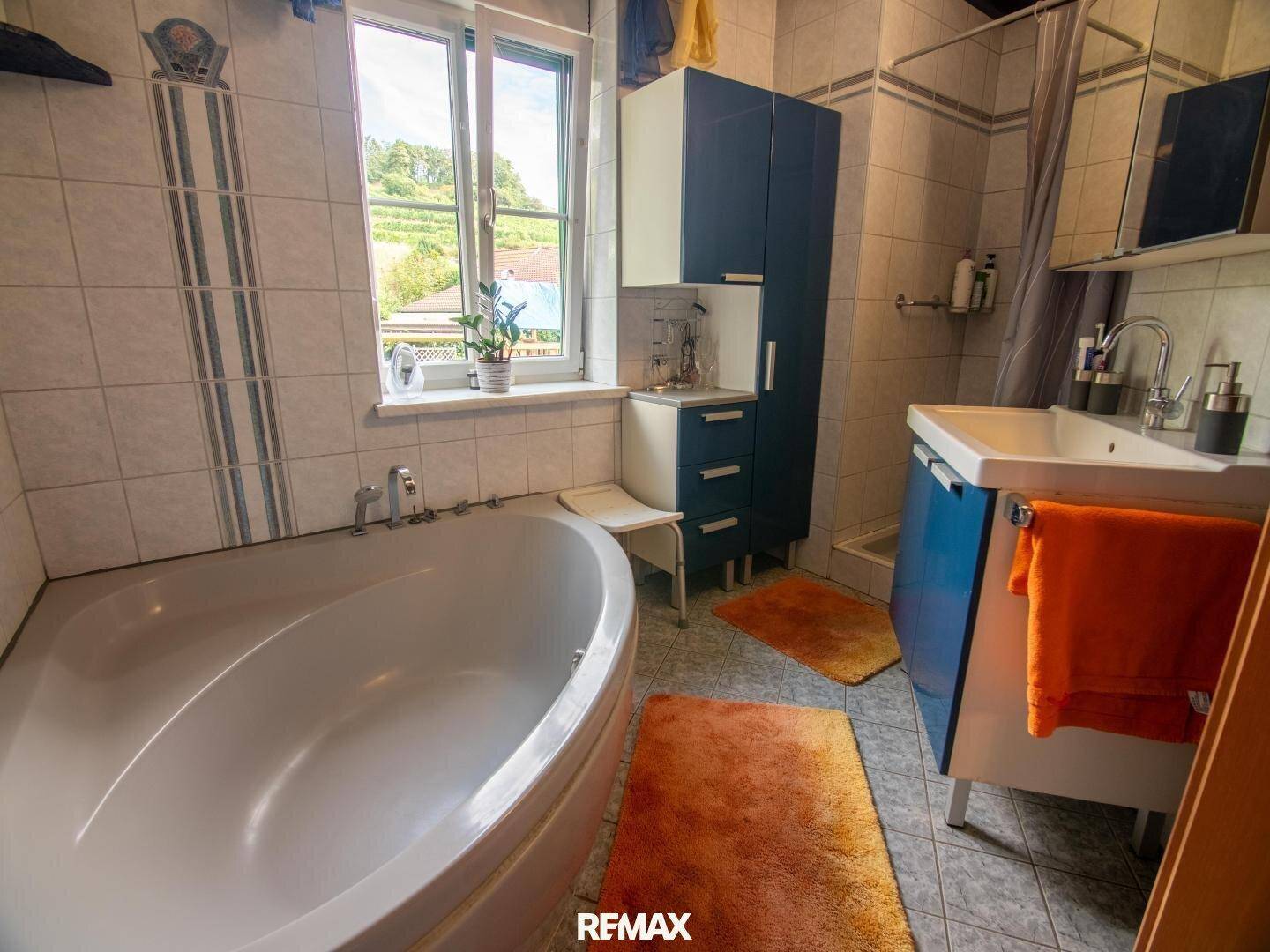 Badezimmer mit Eckbadewanne, Fenster und blauen Schränken.