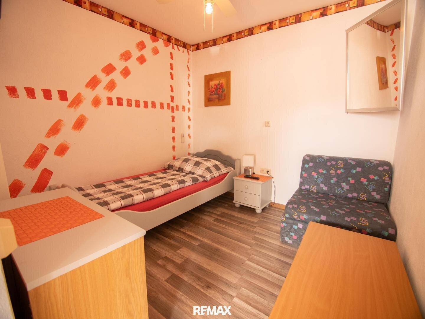Schlafzimmer mit Einzelbett, Holzboden und farbenfroher Wandgestaltung.