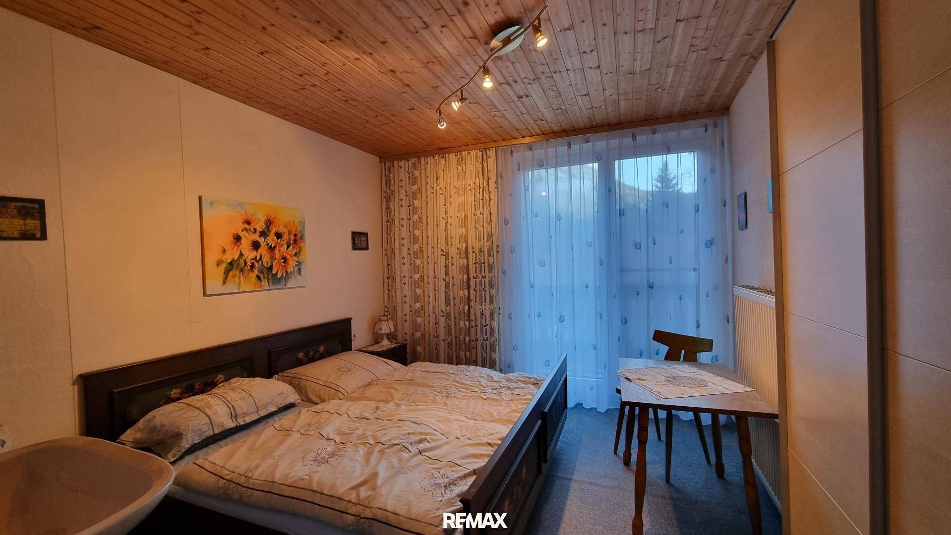 Schlafzimmer mit Doppelbett, Holztäfelung an der Decke und Zugang zum Balkon.