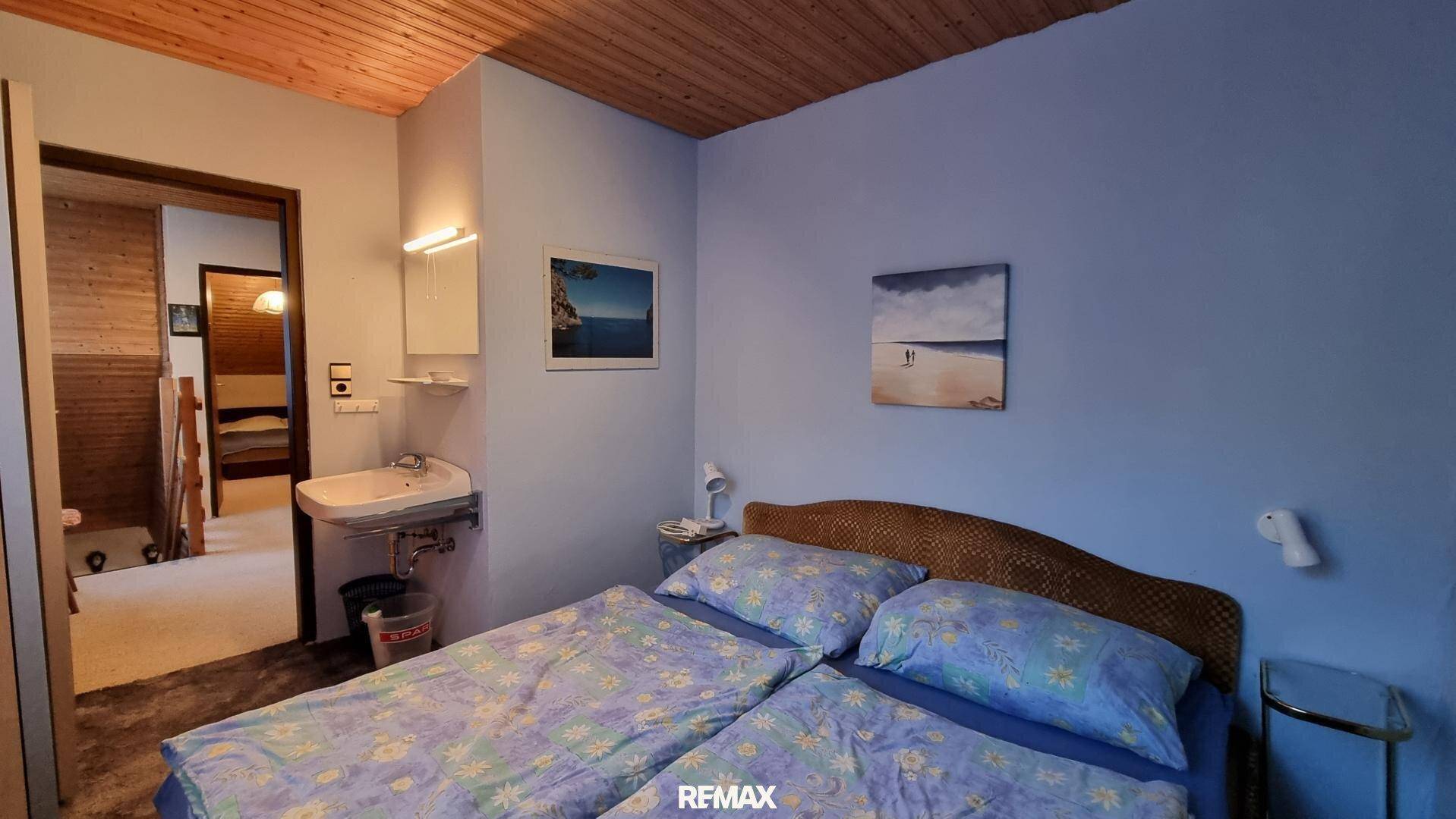 Schlafzimmer mit blau gestrichenen Wänden, Einzelwaschbecken und Holzbalkendecke.