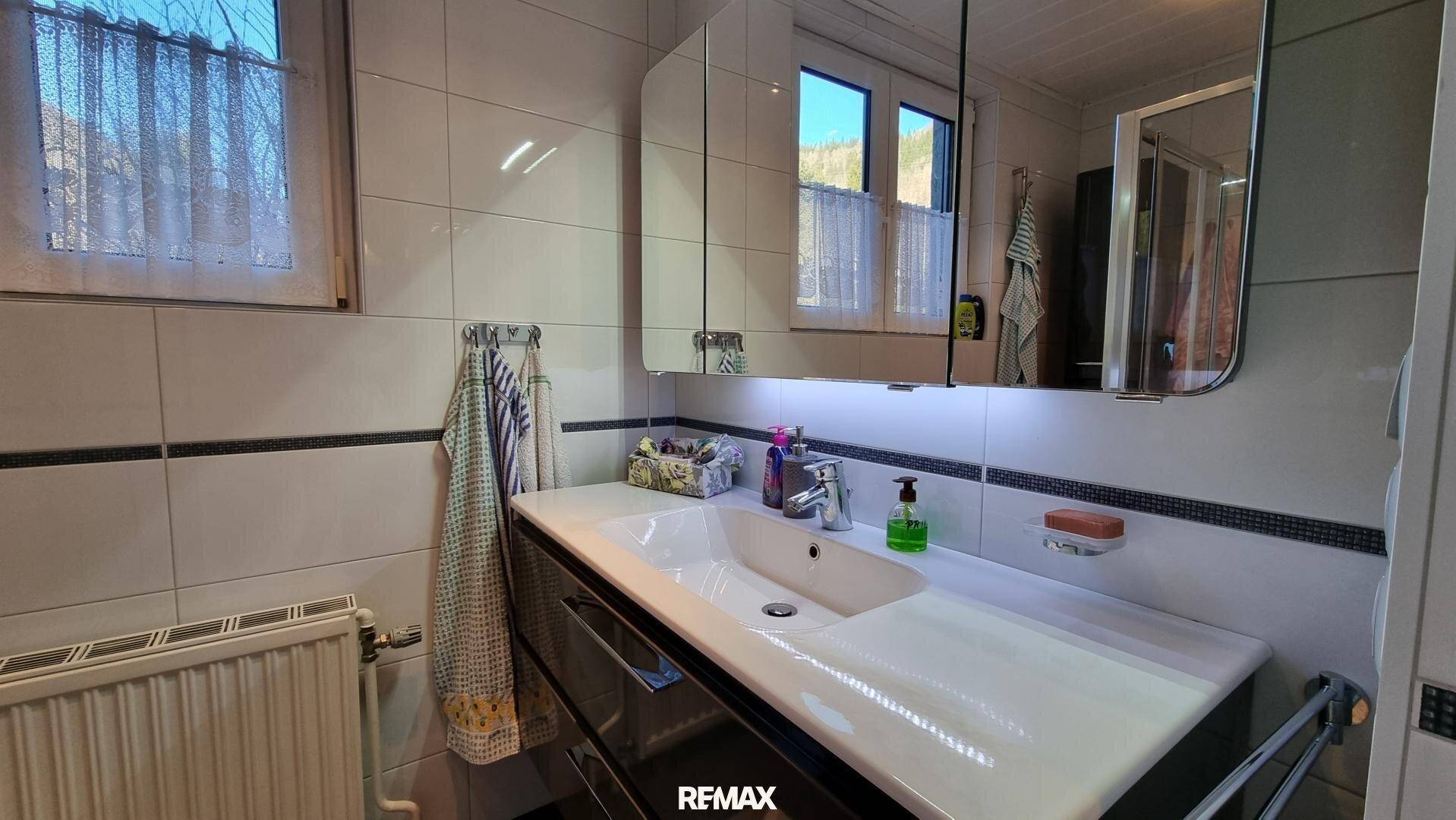 Modernisiertes Badezimmer mit Waschtisch, Spiegelschrank und weißen Fliesen.