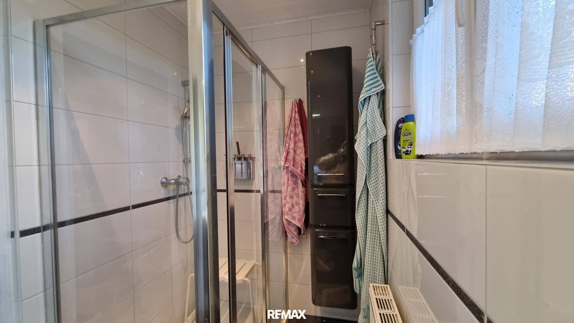 Badezimmer mit Duschkabine, weißen Fliesen und kleinem Fenster für Tageslicht.