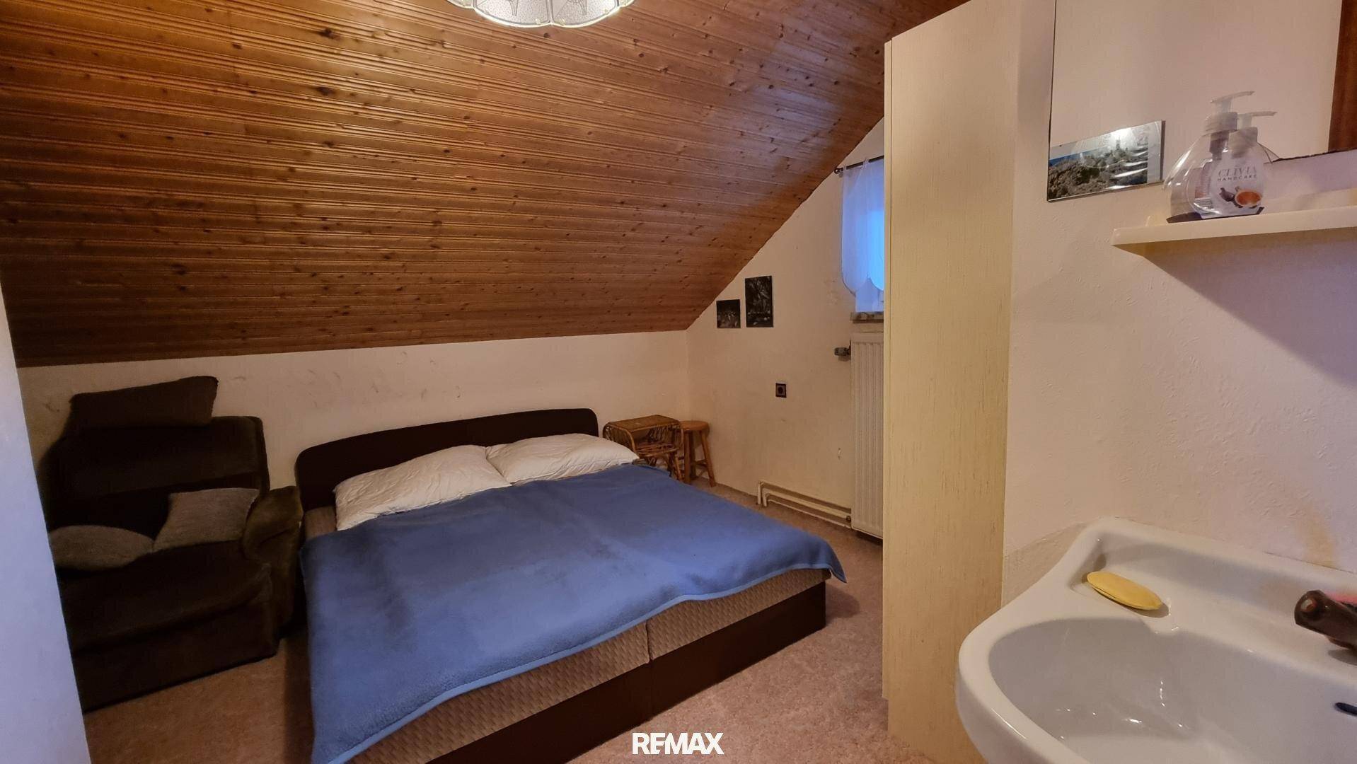 Dachgeschoss-Schlafzimmer mit Holztäfelung, Dachschräge und integriertem Waschbecken.