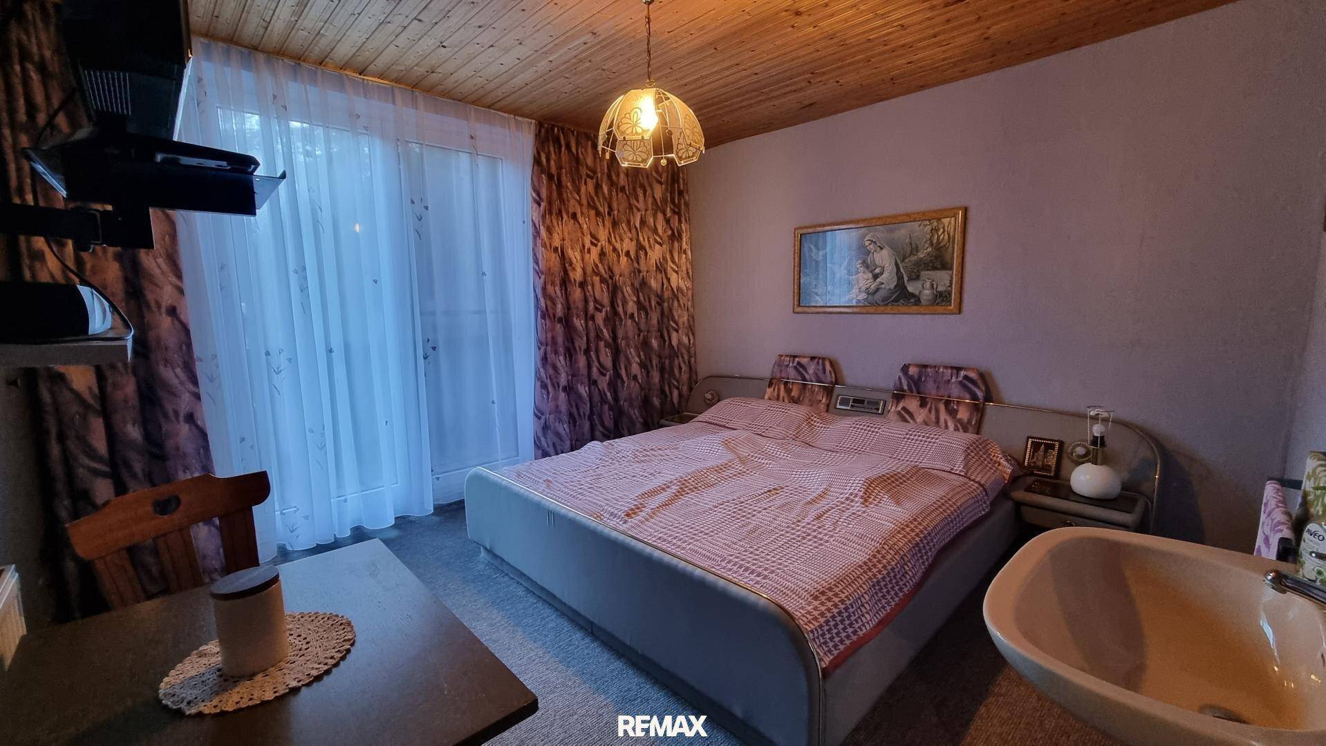 Schlafzimmer mit Doppelbett, Holztäfelung an der Decke und Zugang zum Balkon.