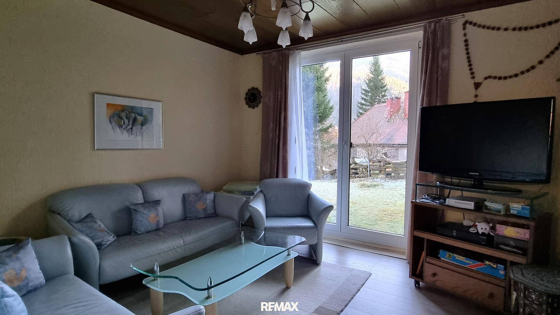 Helles Wohnzimmer mit beiger Couch, Holzbalkendecke und Blick in den Garten.