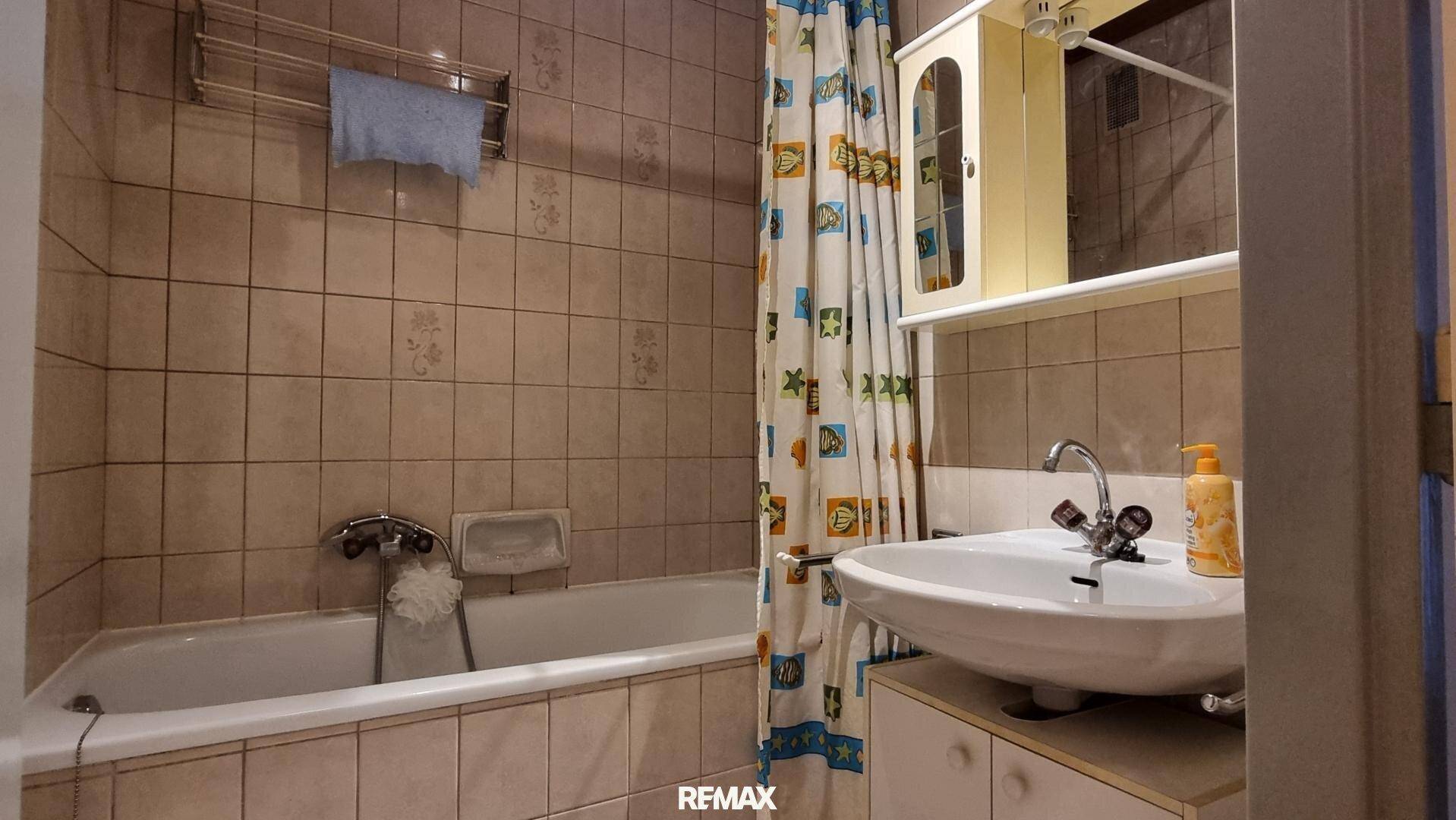 Badezimmer mit Badewanne, Waschbecken und beigefarbenen Fliesen an den Wänden.