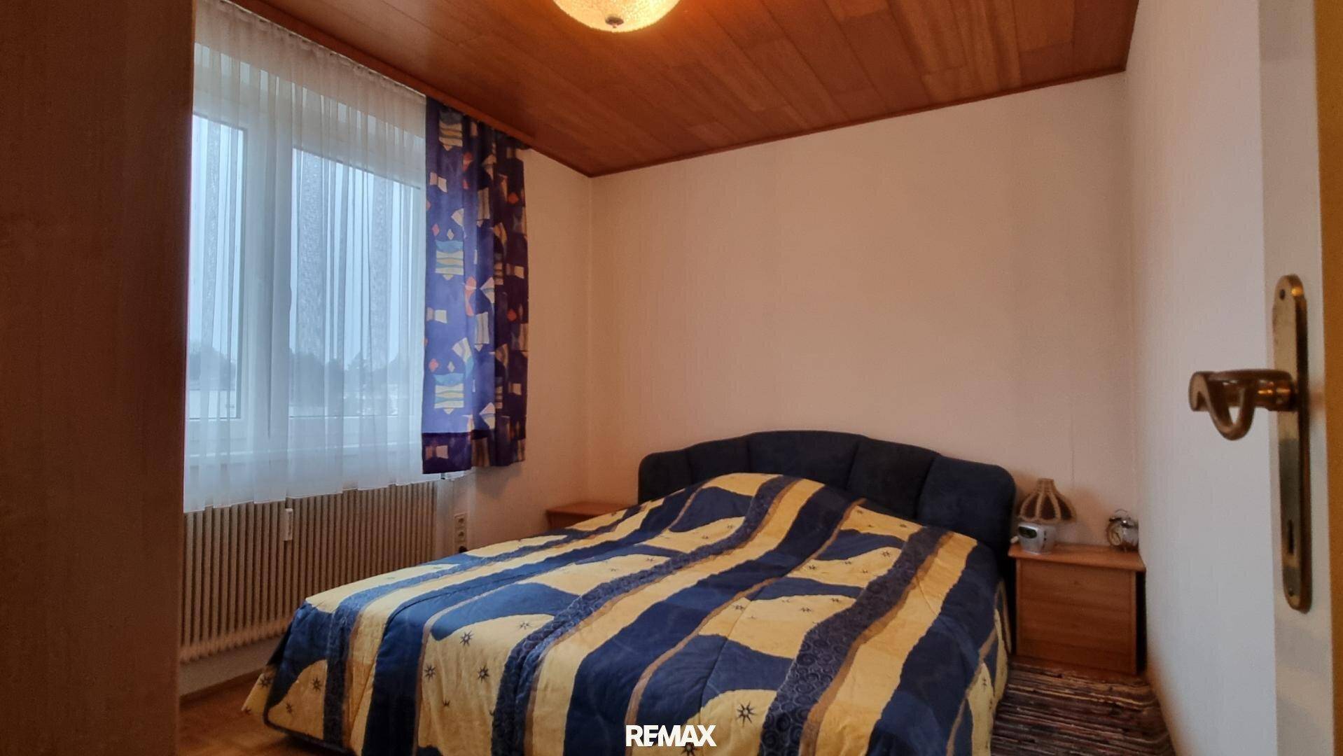 Schlafzimmer mit Doppelbett, Holzdecke und Fenster mit Vorhängen.