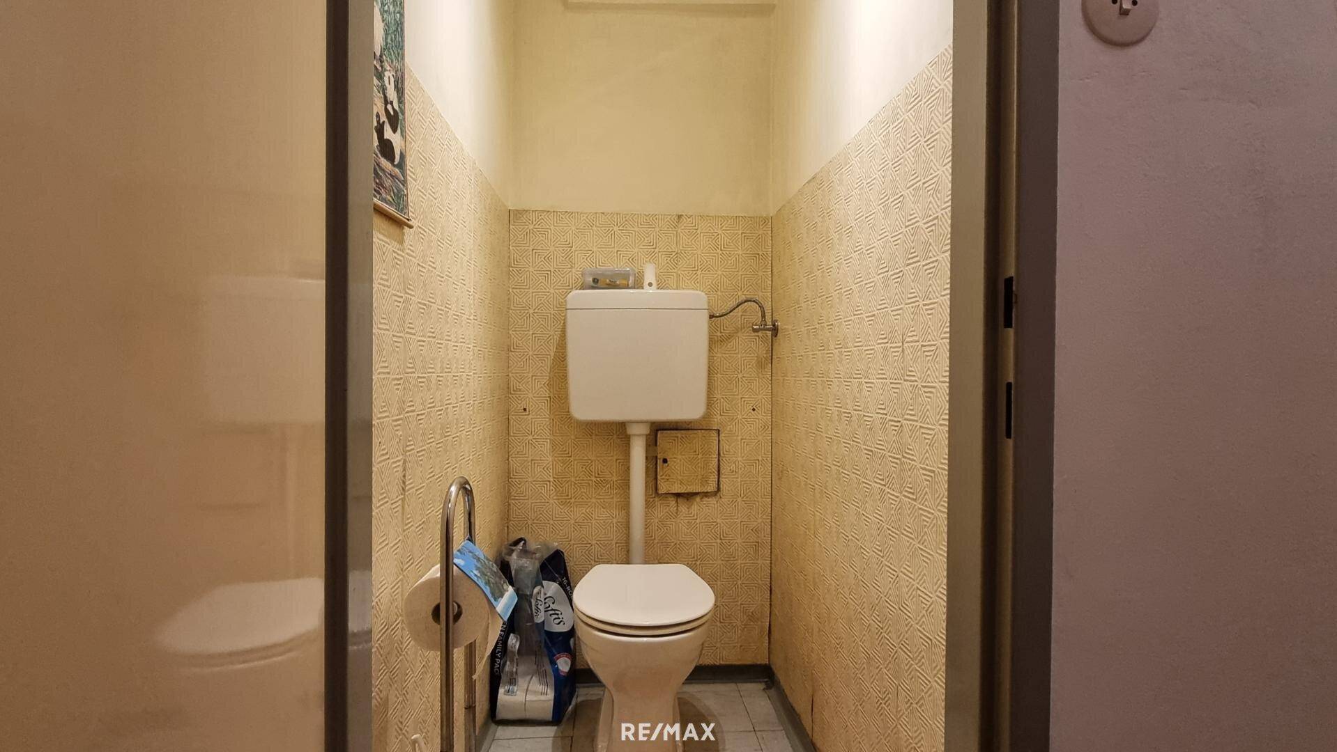 Separate Toilette mit WC und einfachen Fliesen im oberen Wandbereich.