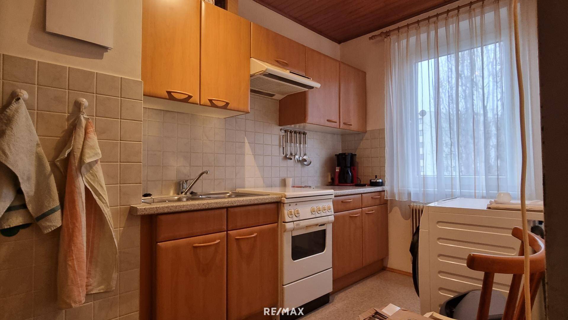 Funktionale Küche mit Holzschränken, Fliesenrückwand und einem Fenster für Tageslicht.