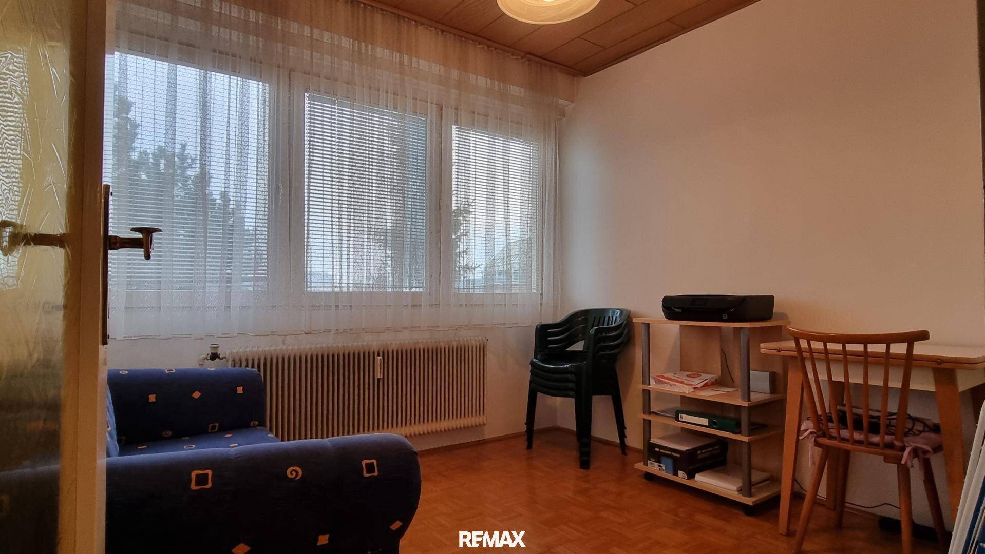 Helles Zimmer mit Schreibtisch, Stuhl, Holzdecke und großem Fenster.