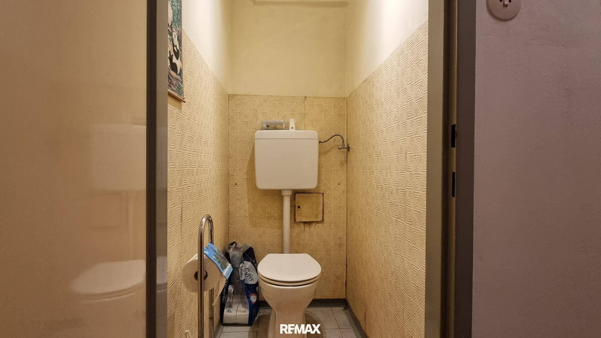 Separates WC mit wandmontierter Toilette und gemusterter Tapete.