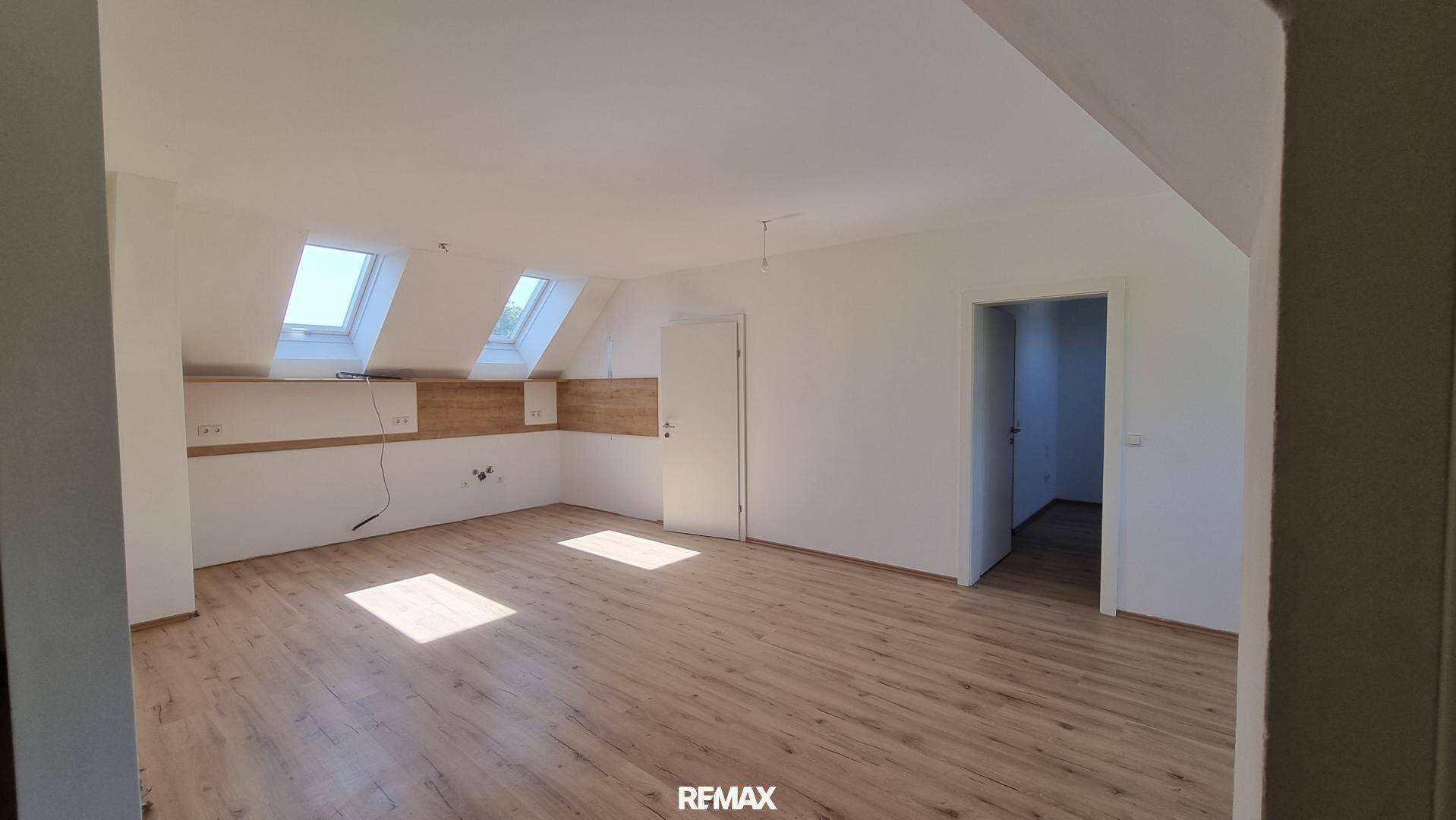 Geräumiger Wohnbereich mit hellem Laminatboden, weißen Wänden und mehreren Dachfenstern für viel Helligkeit.
