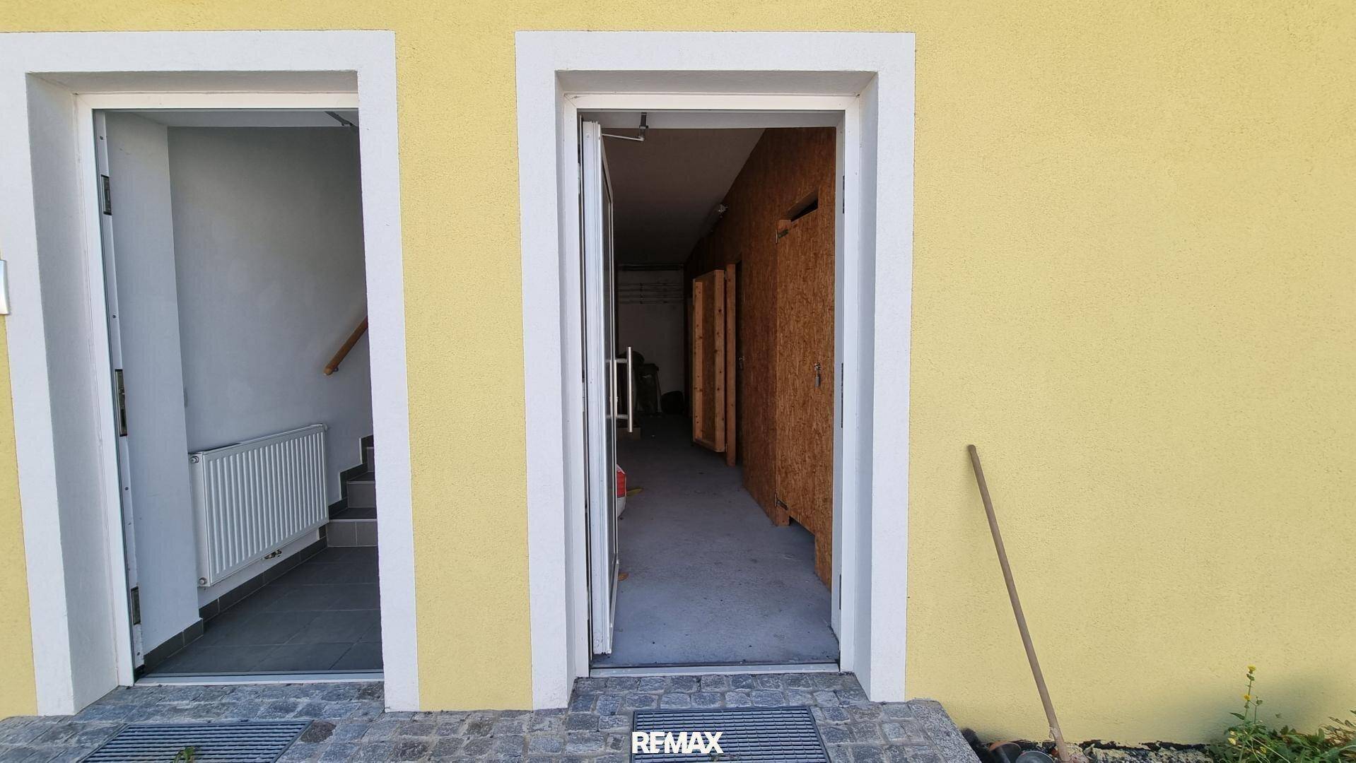 Eingangsbereich eines Gebäudes mit gelber Fassade und zwei Türen, eine davon offen, gepflegter Zustand.