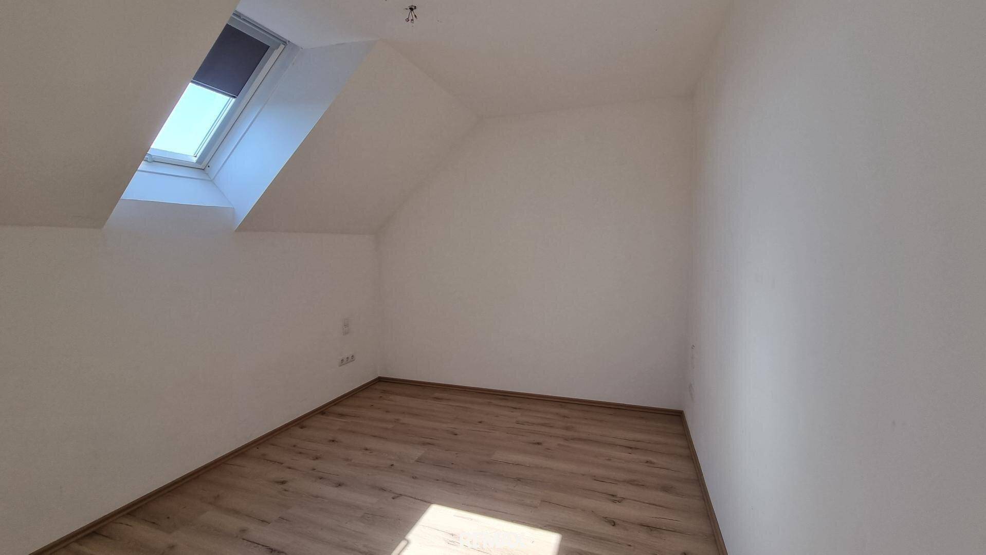 Helles Schlafzimmer mit Laminatboden, weißen Wänden und einem Dachfenster, das für eine angenehme Atmosphäre sorgt.