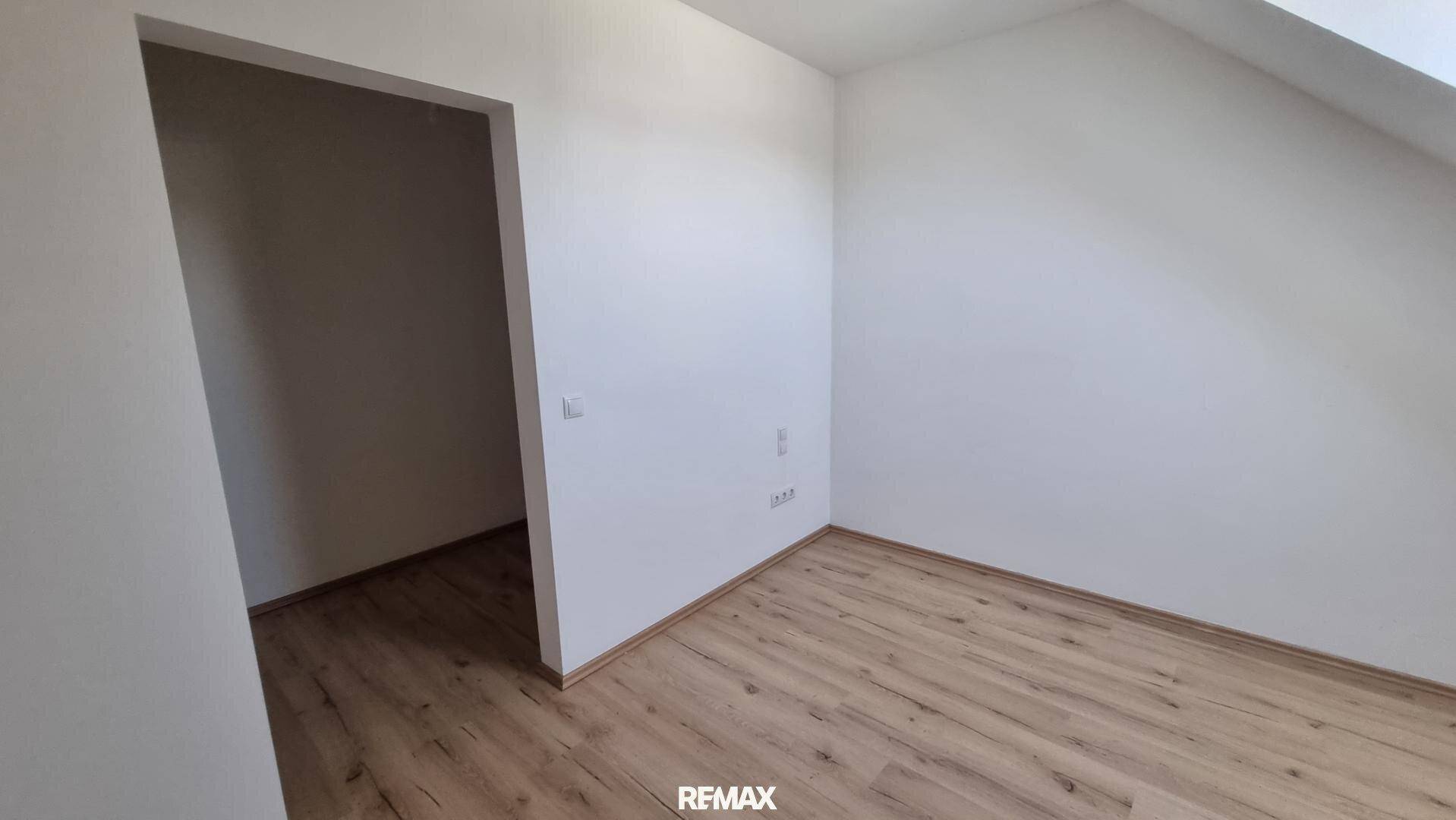 Kleineres Zimmer mit hellem Laminatboden und weißen Wänden, das durch eine offene Tür zugänglich ist.