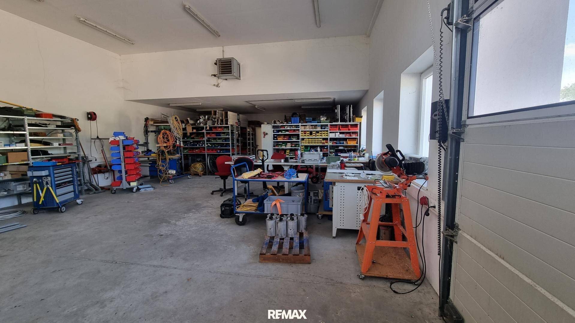 Große Werkstatt mit Rolltor, Werkbänken und Regalen, viel Platz für verschiedene Arbeiten.