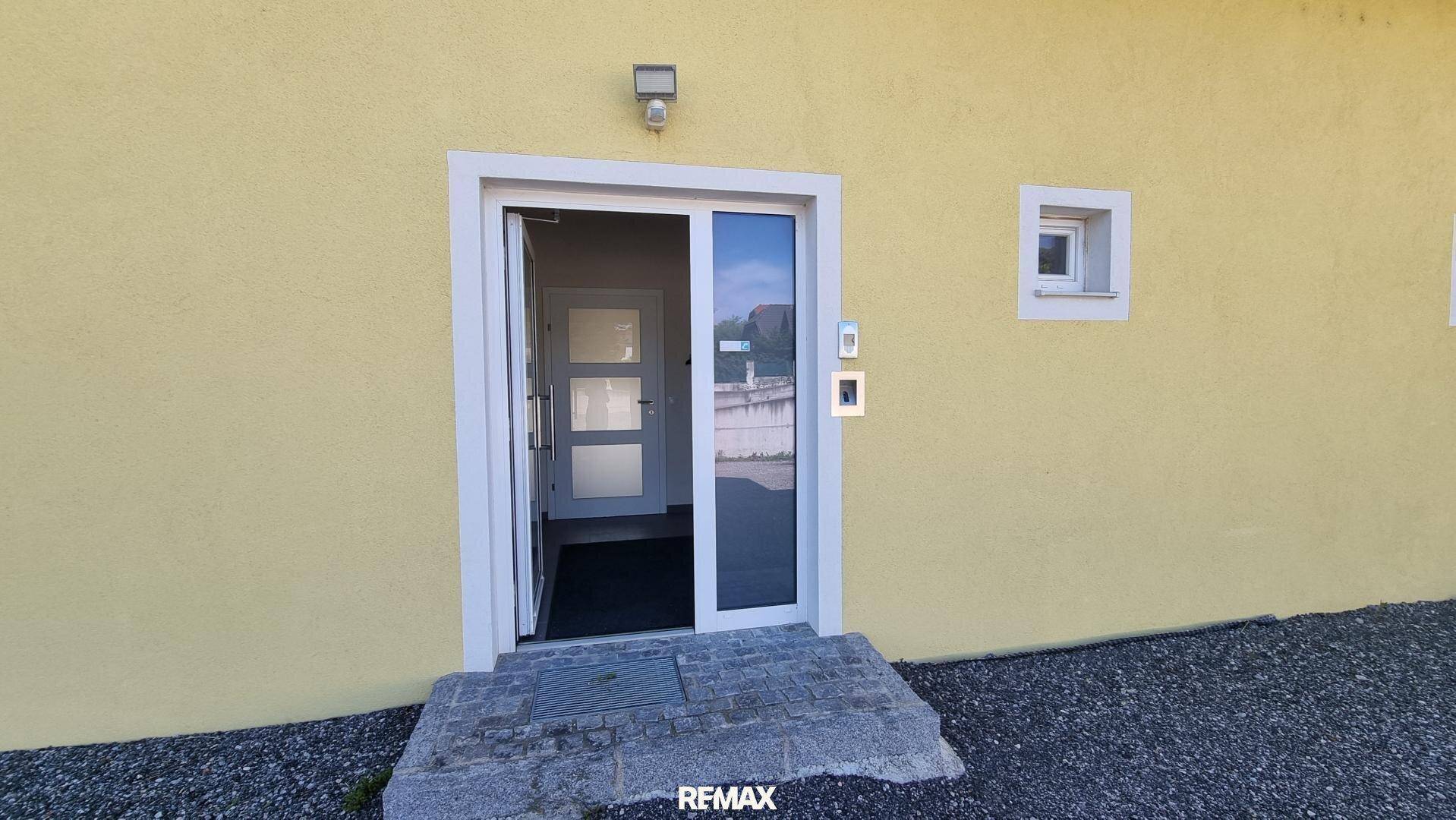 Eingangsbereich eines Gebäudes mit gelber Fassade und moderner Glastür, sauber und gepflegt.