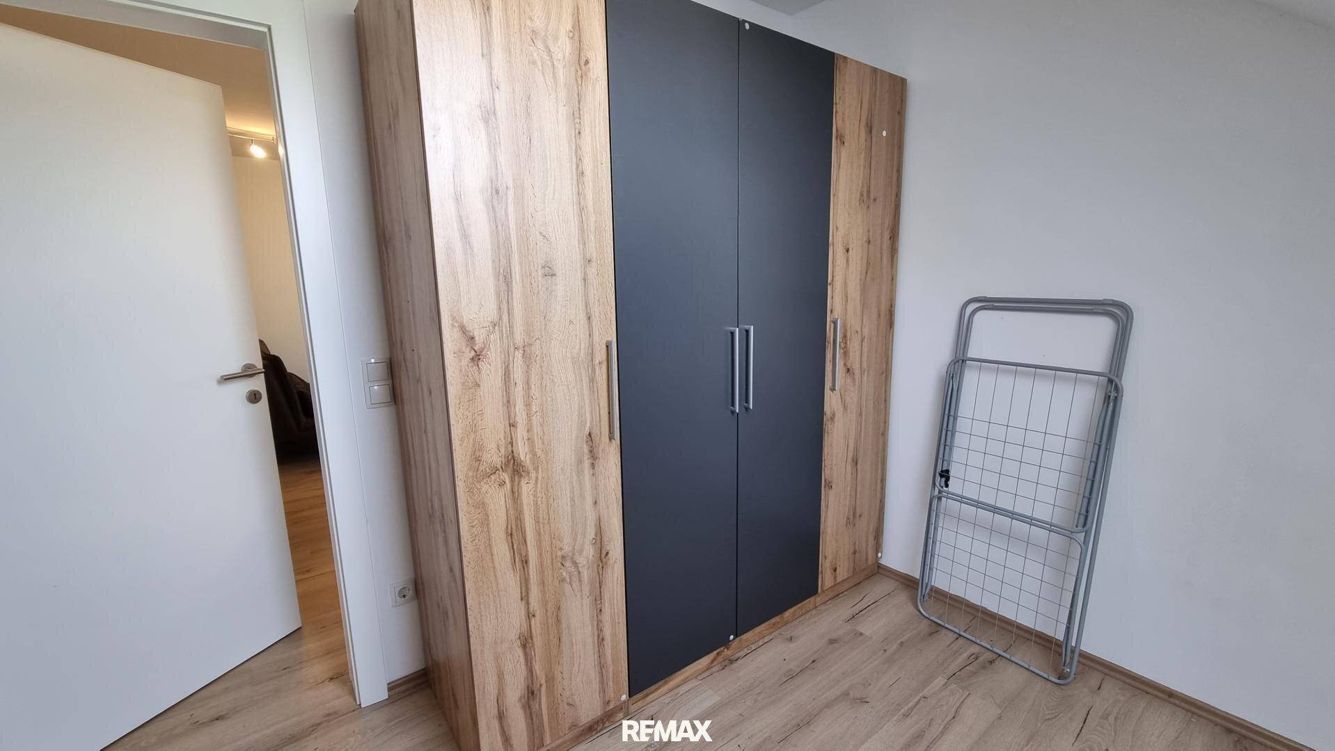 Schlafzimmer mit großem Kleiderschrank in Holz- und Anthrazitoptik, ergänzt durch hellen Laminatboden.