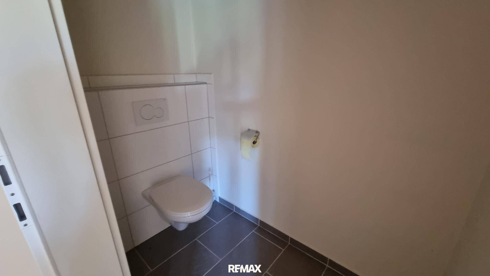 Kleiner Toilettenraum mit wandhängendem WC und dunklen Bodenfliesen, in einem sauberen Zustand.
