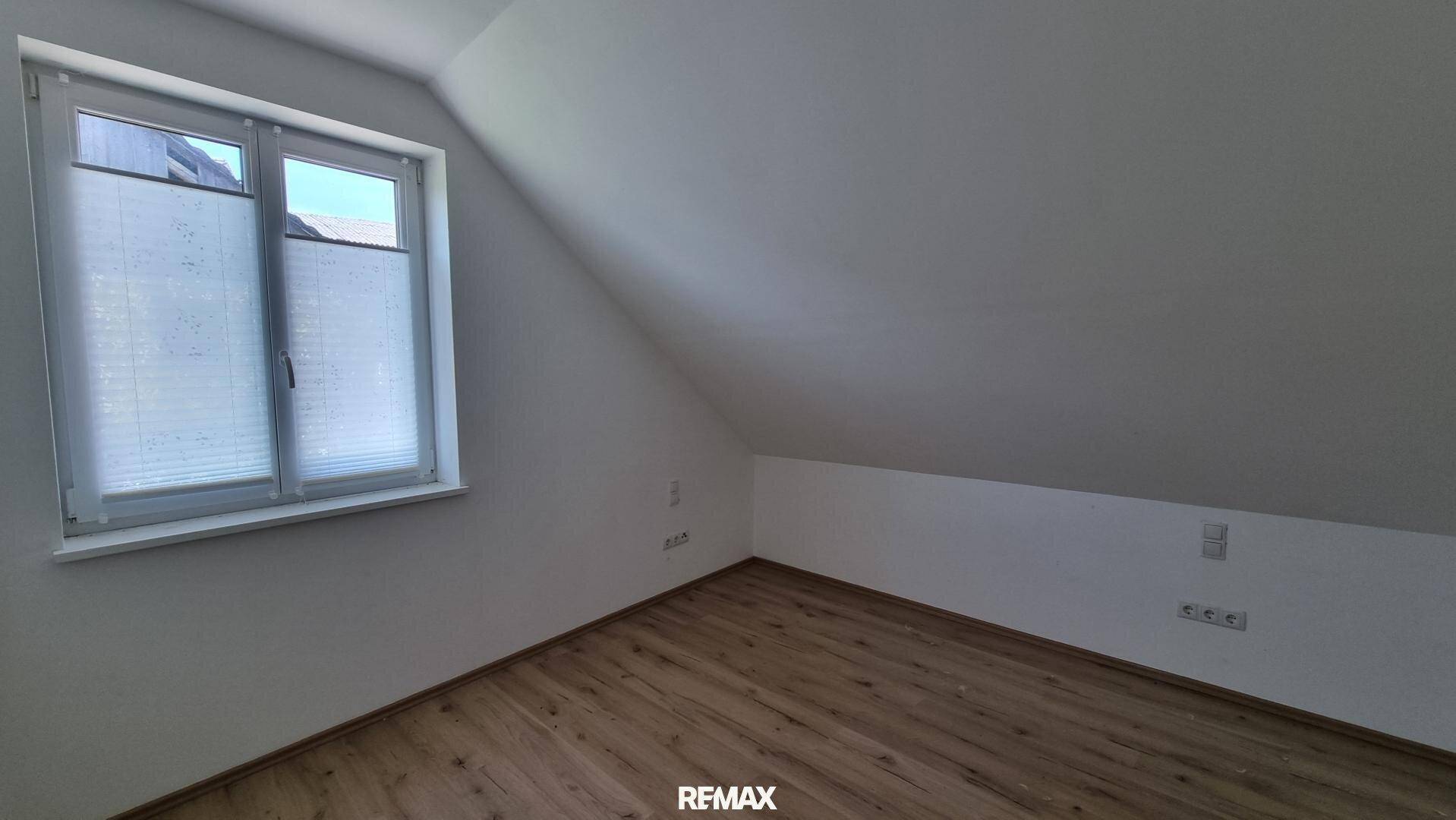 Schlafzimmer im Dachgeschoss mit schräger Decke und Fenster, ausgestattet mit hellem Laminatboden.