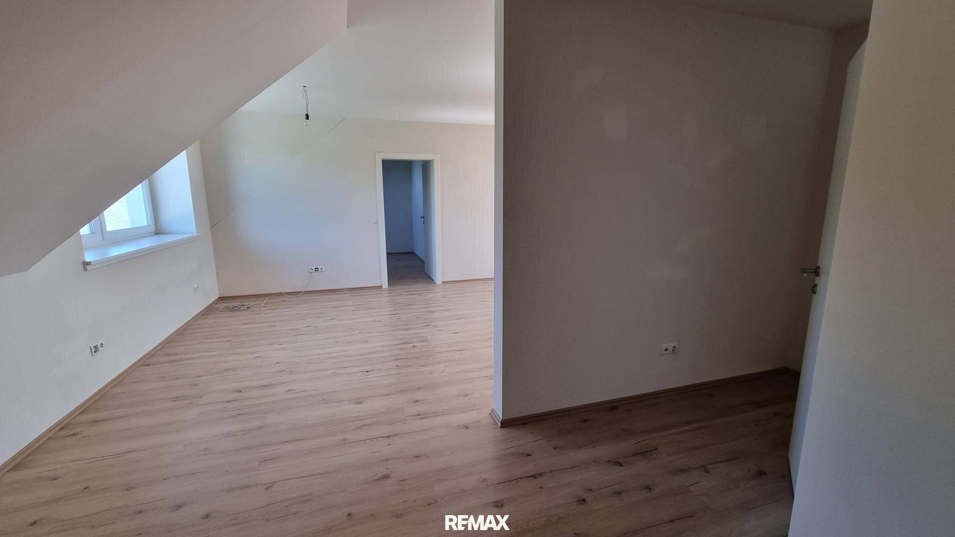 Geräumiger Wohnbereich mit hellem Laminatboden und weißen Wänden, der einen offenen Grundriss bietet.