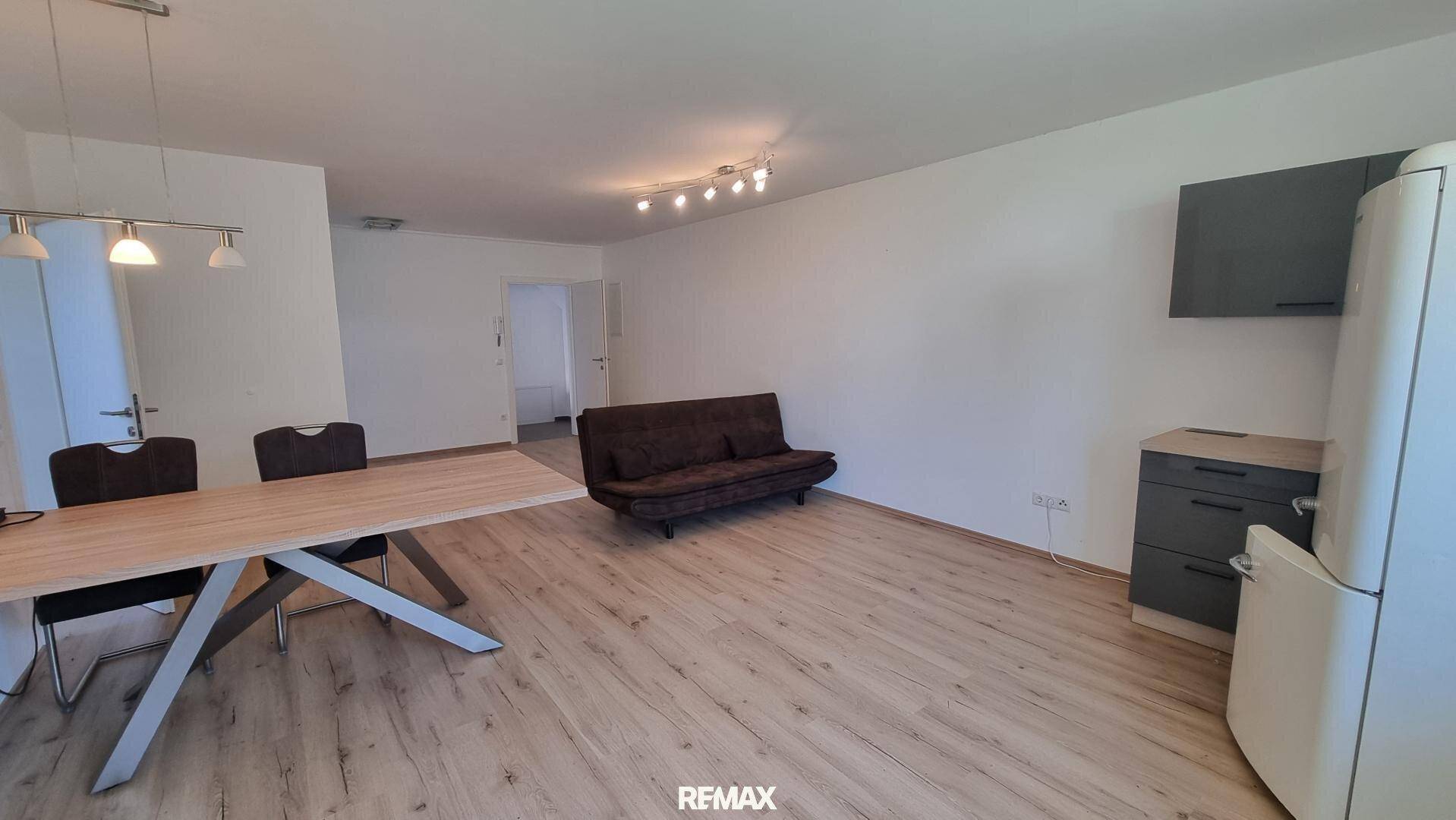 Geräumiger Wohn- und Essbereich mit hellem Laminatboden, Sofa und Esstisch, offen gestaltet.