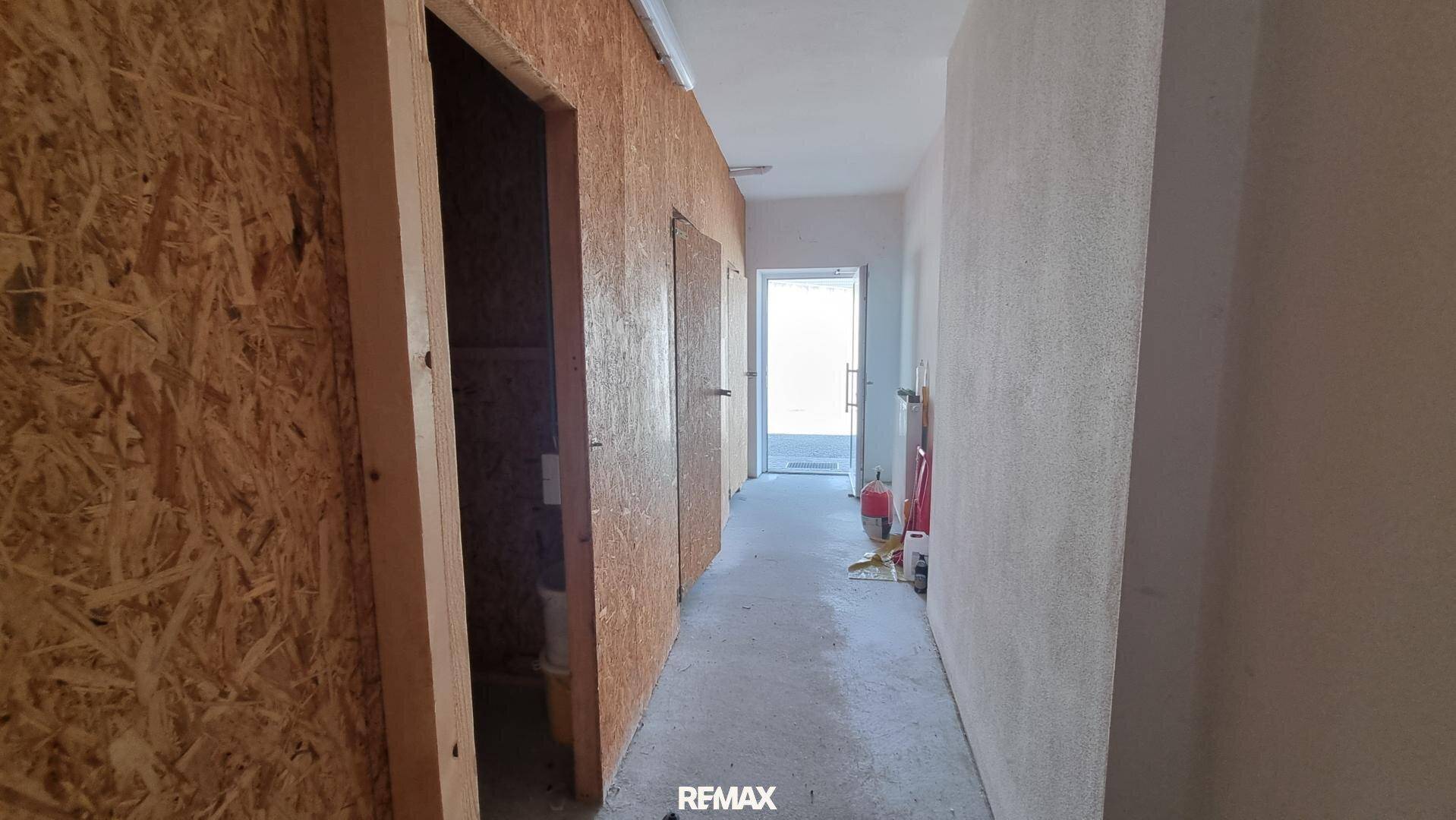 Flur mit OSB-Platten und weiß verputzter Wand, Blick zum Eingangsbereich, einfacher Ausbau.