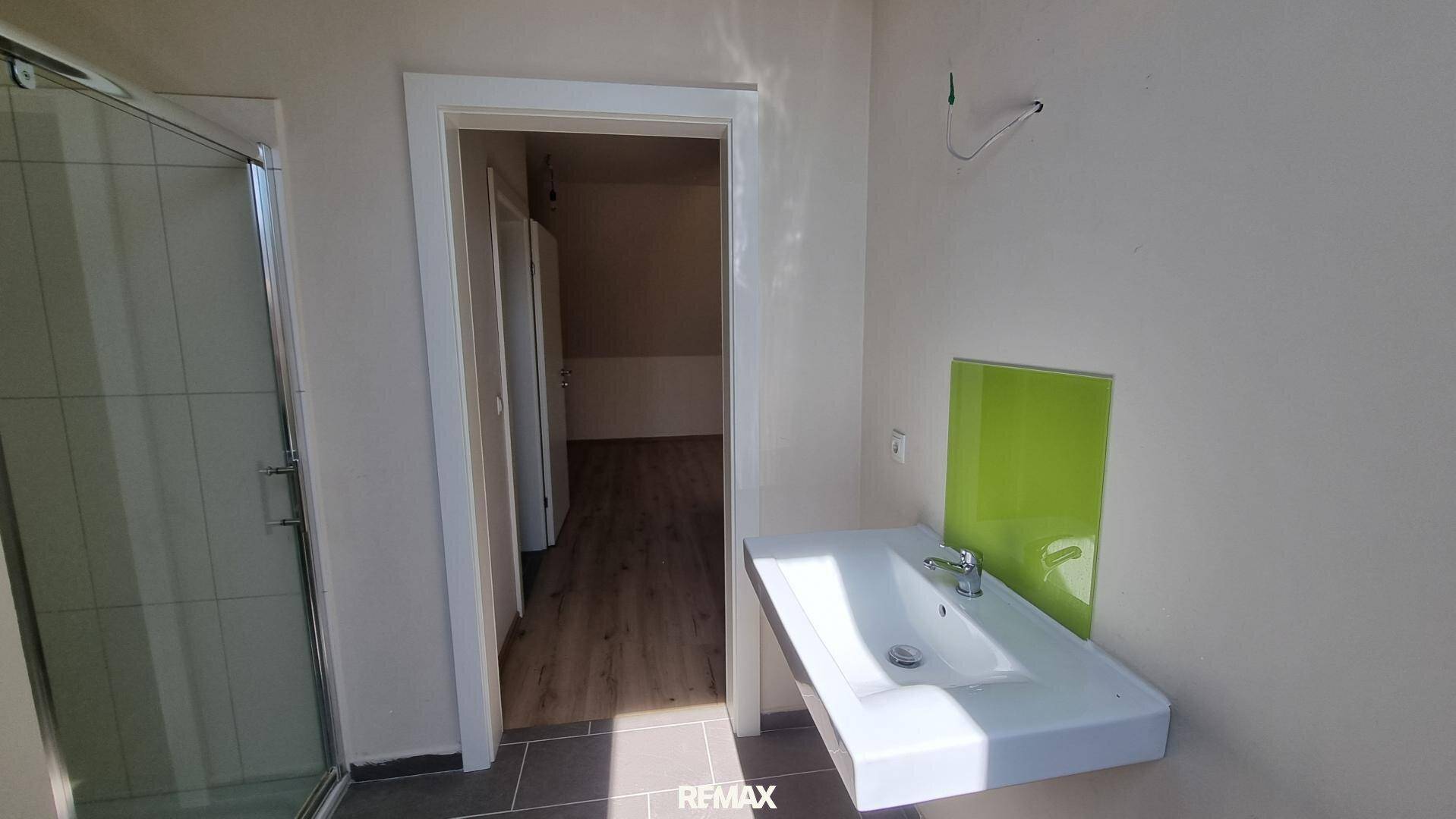 Badezimmer mit Duschkabine, Waschbecken und dunklen Fliesen, akzentuiert durch eine grüne Wandverkleidung.