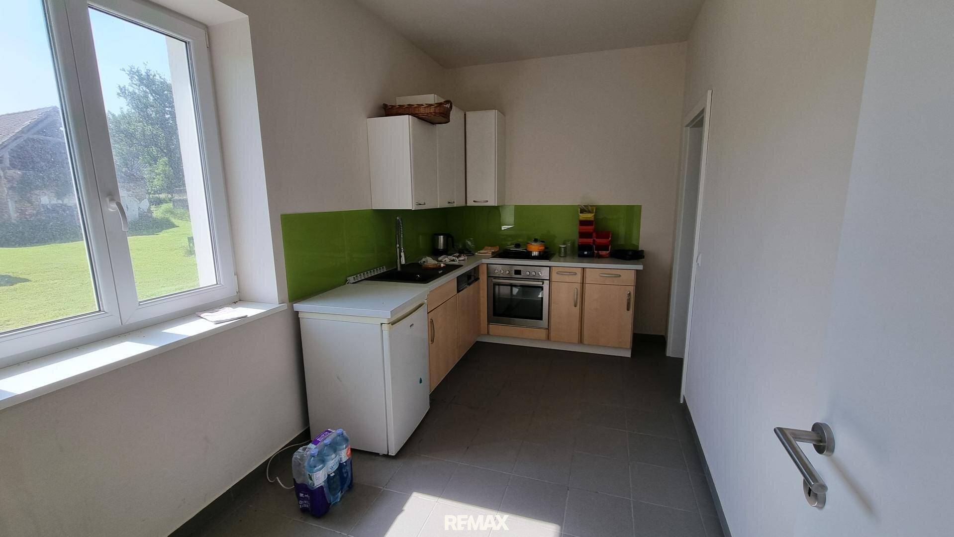 Kleine Küche mit Einbauschränken, Spüle, Herd und Fenster mit Blick ins Grüne, funktional.