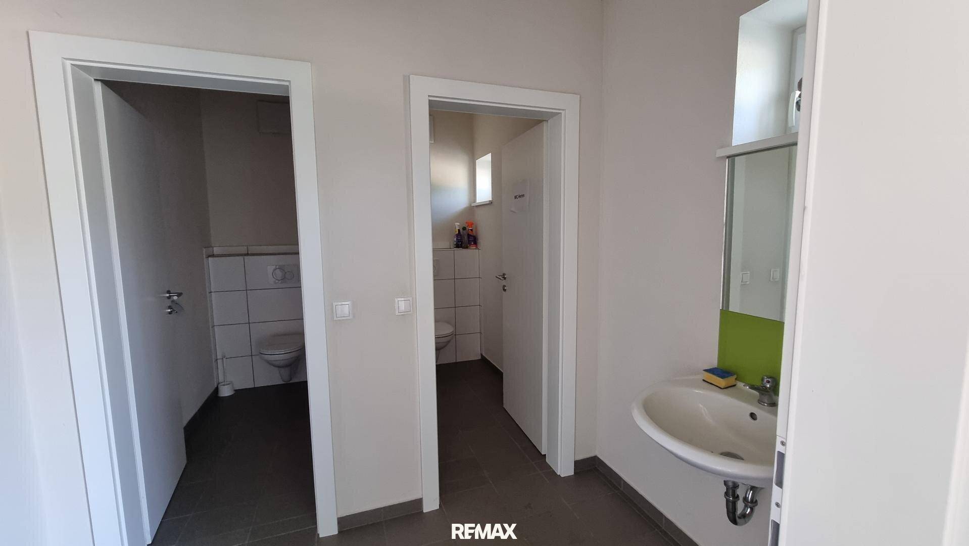 Zwei separate Toilettenräume und ein Waschbeckenbereich mit Spiegel und Fenster, funktional eingerichtet.