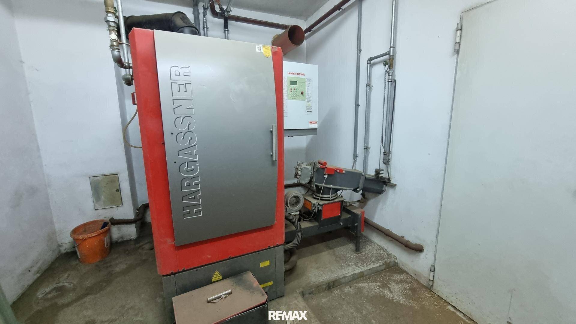 Heizungsraum mit einem großen roten Hargassner-Heizkessel und sichtbaren Rohrleitungen an den Wänden.
